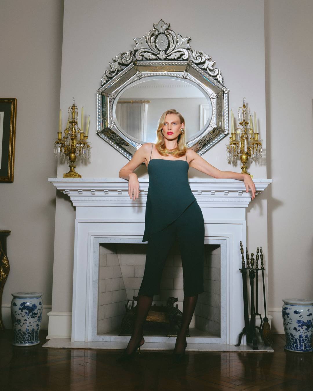 Pessoa com vestido verde elegante, inspirando a moda dos anos 80 e 90, em frente a uma lareira com espelho.