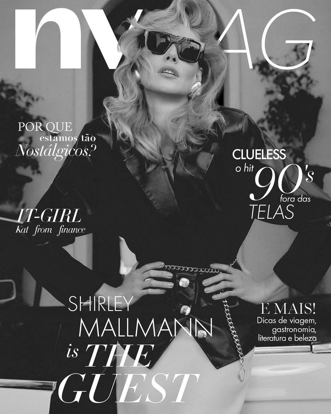 Modelo com cabelo volumoso no estilo da moda dos anos 80 e 90, usando óculos escuros, blazer preto e acessórios grandes.