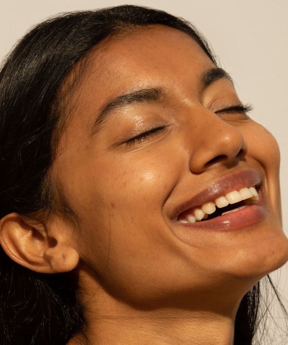 Mulher sorrindo com pele brilhante e suave, evidenciando efeito glass skin.