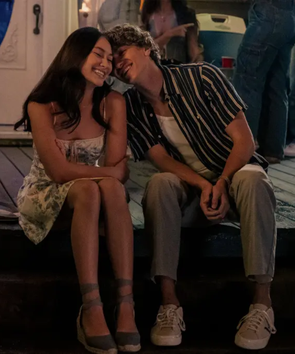Um casal jovem sentado em uma escada, sorrindo enquanto conversam de maneira carinhosa.