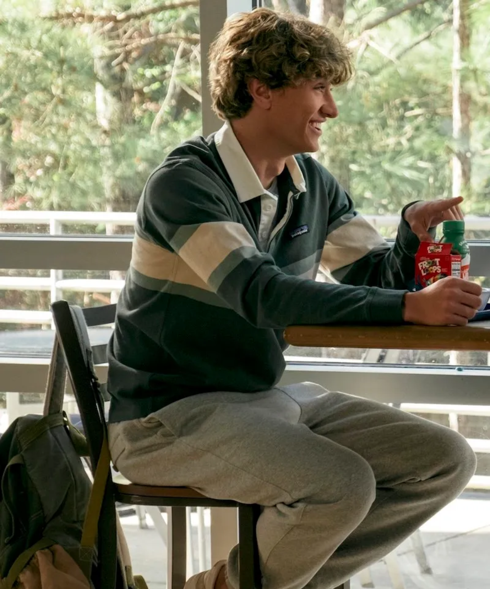 Um jovem sorridente sentado em cafeteria, vestindo suéter listrado.
