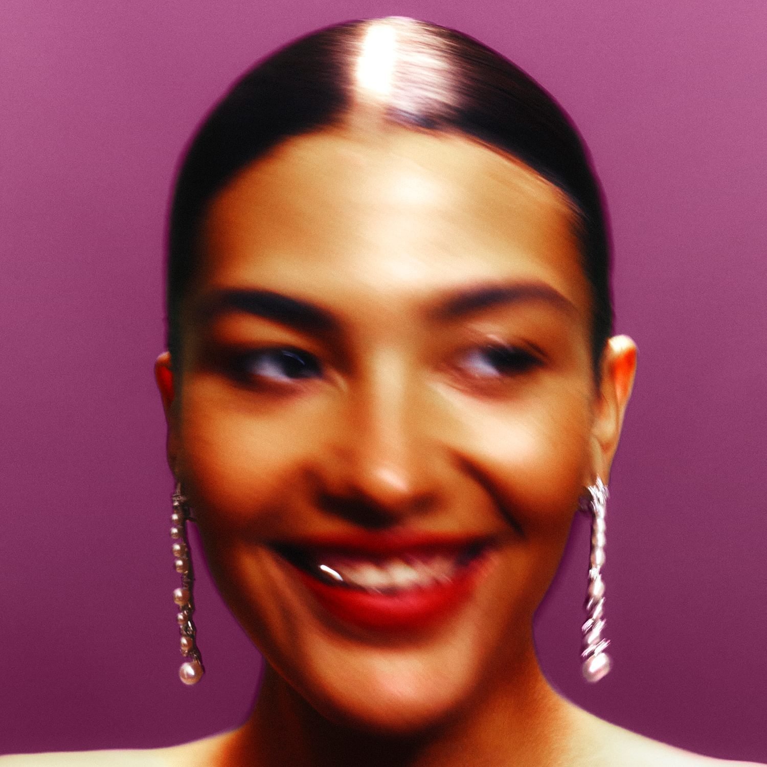 Pessoa sorrindo desfocada em fundo roxo, usando brincos longos.