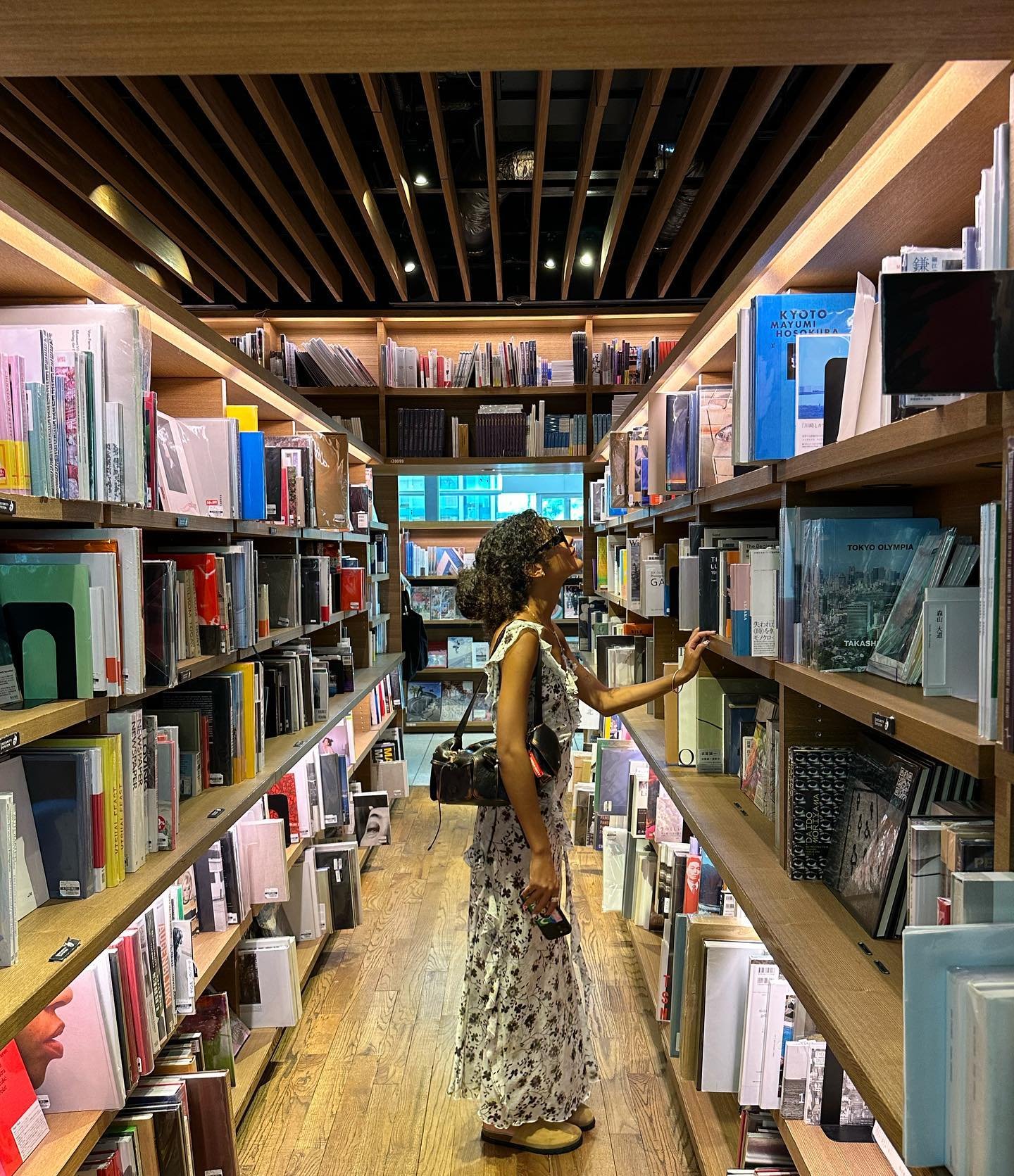 Jovem de vestido floral explora seção de livros em livraria iluminada.