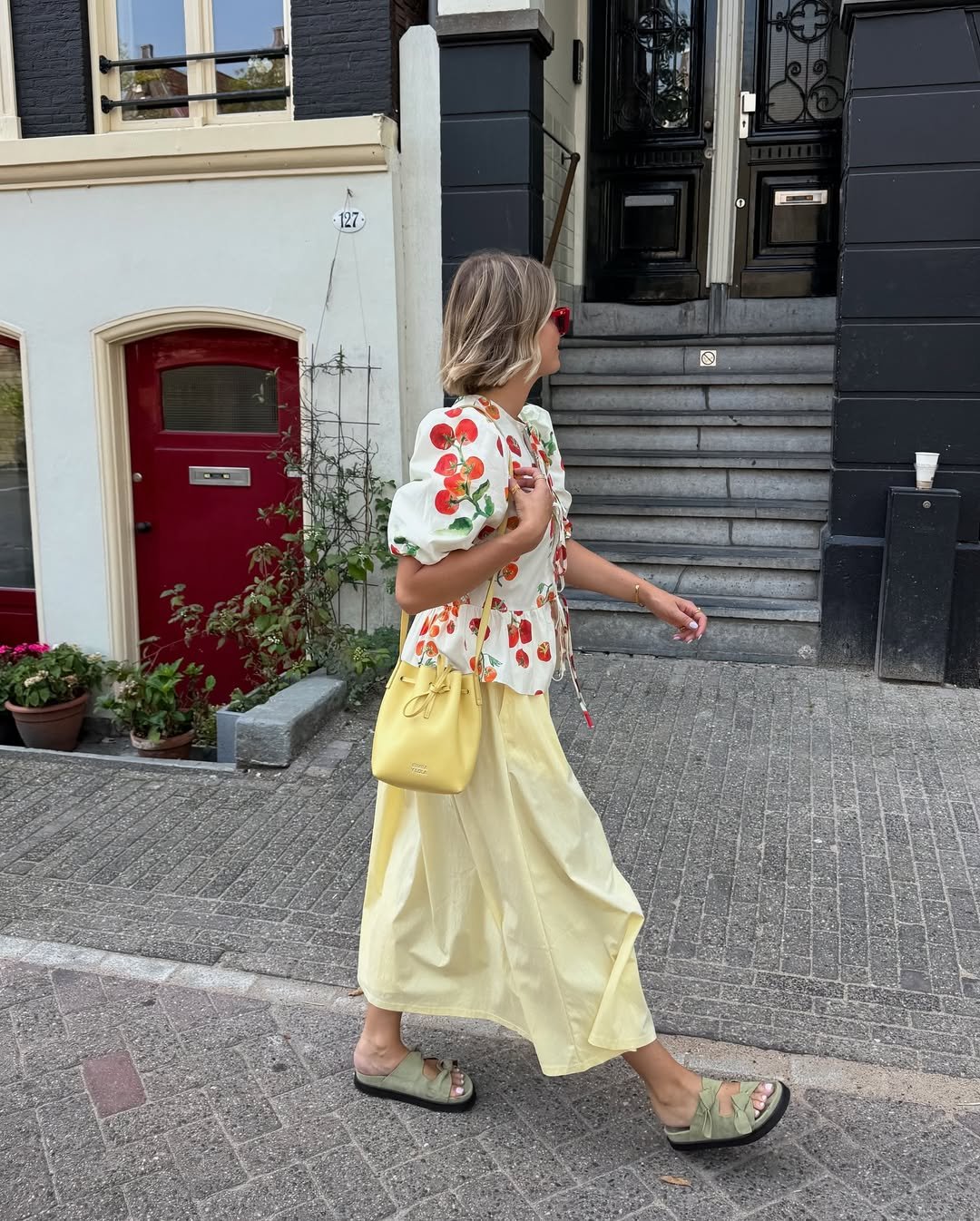 Mulher com blusa estampada e saia amarela caminha em frente a uma casa, usando modelos de papetes confortáveis.