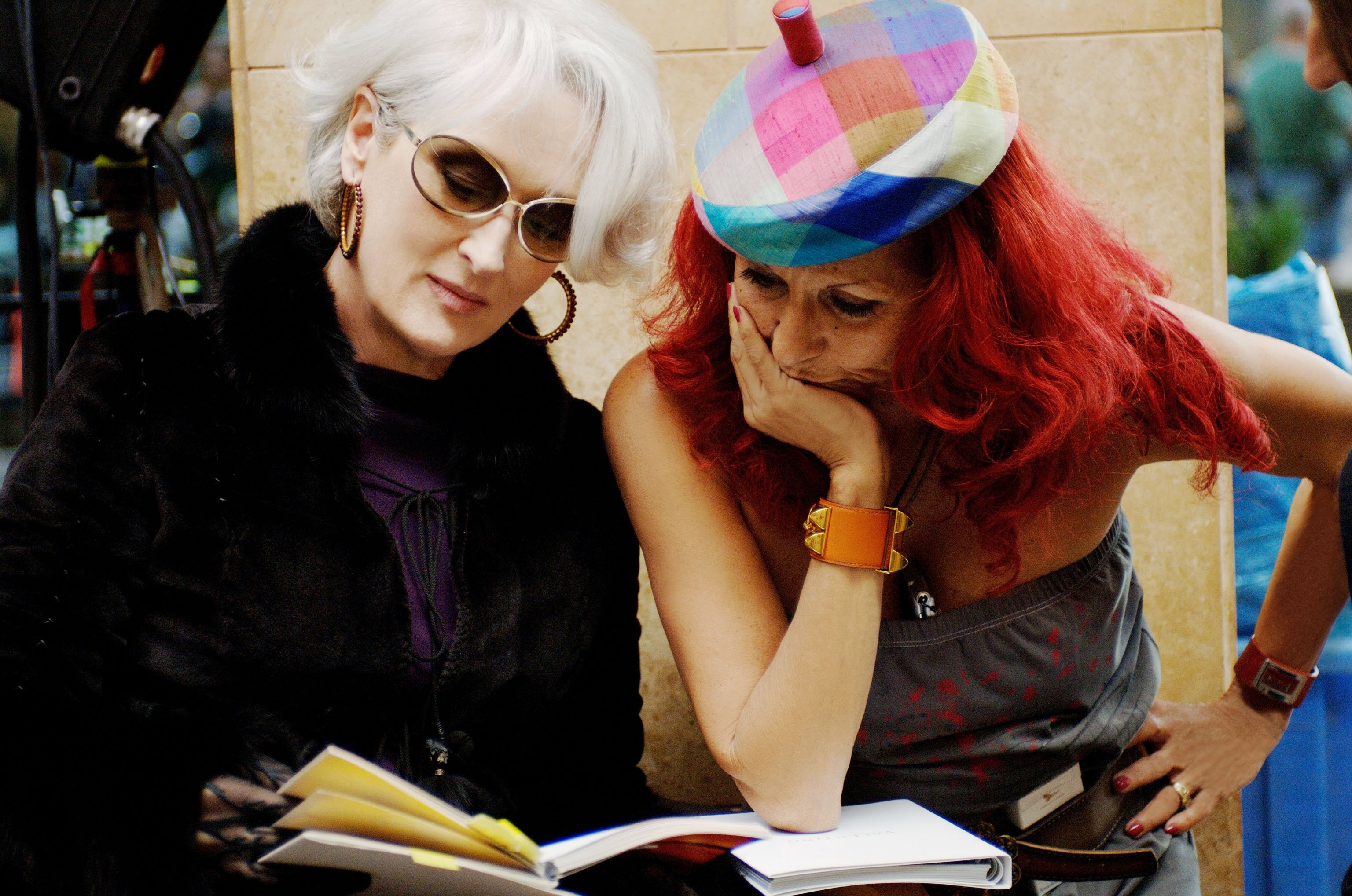 Duas mulheres examinando documentos atentamente. Uma usa boina colorida.