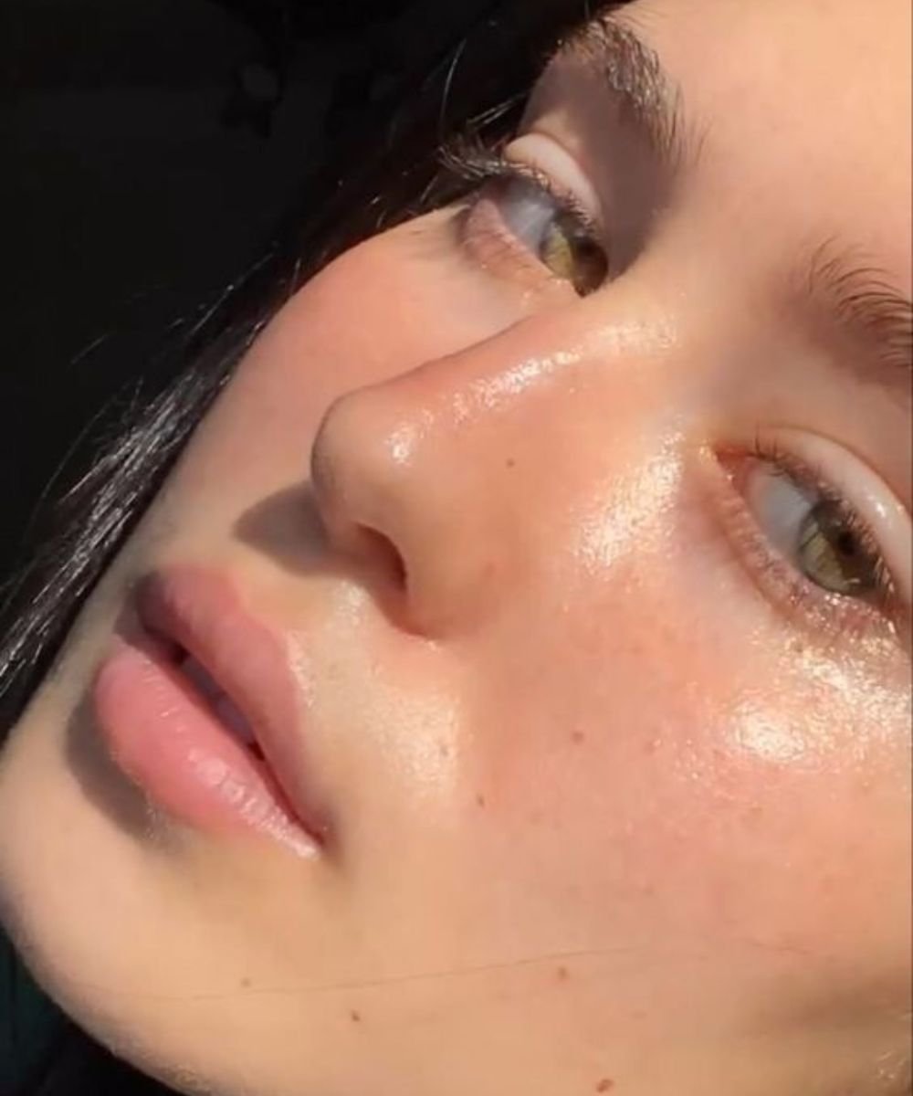 Rosto em close exibindo pele brilhante e uniforme, sugerindo pele oleosa tratata e bem hidratada sob luz direta.