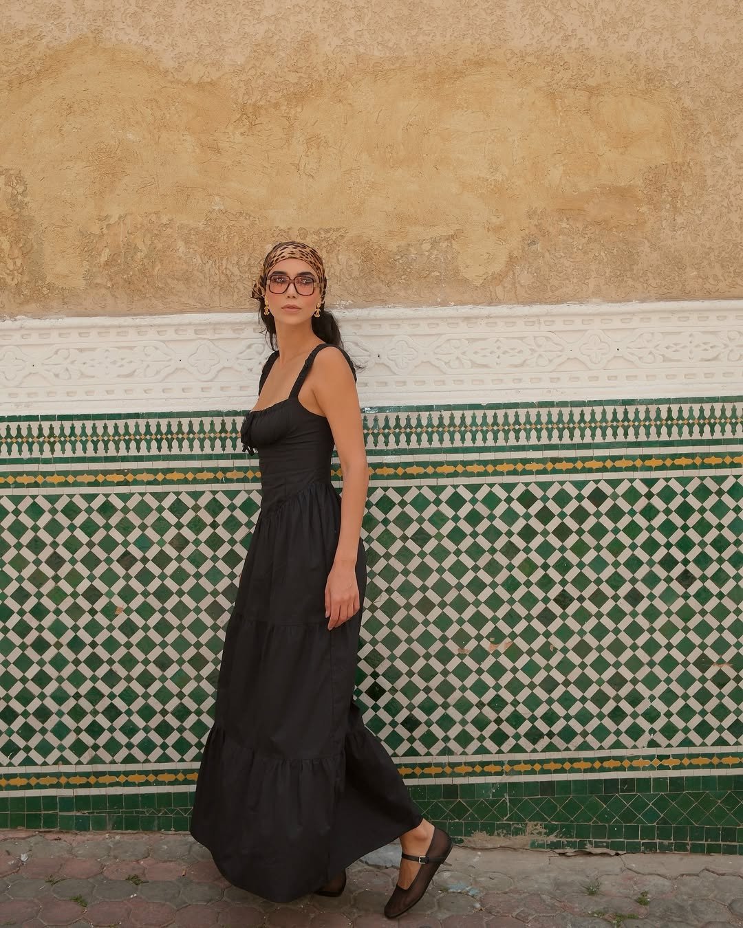 Mulher em vestido preto passa por parede com azulejos, ilustrando um dos melhores perfumes árabes femininos