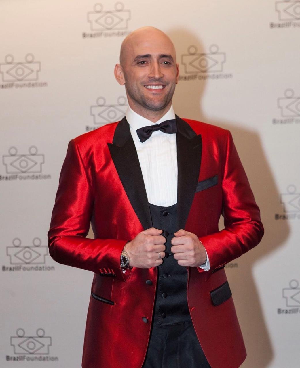 Leilão Paulo Gustavo orrindo em um evento, usando paletó vermelho brilhante com detalhe preto.