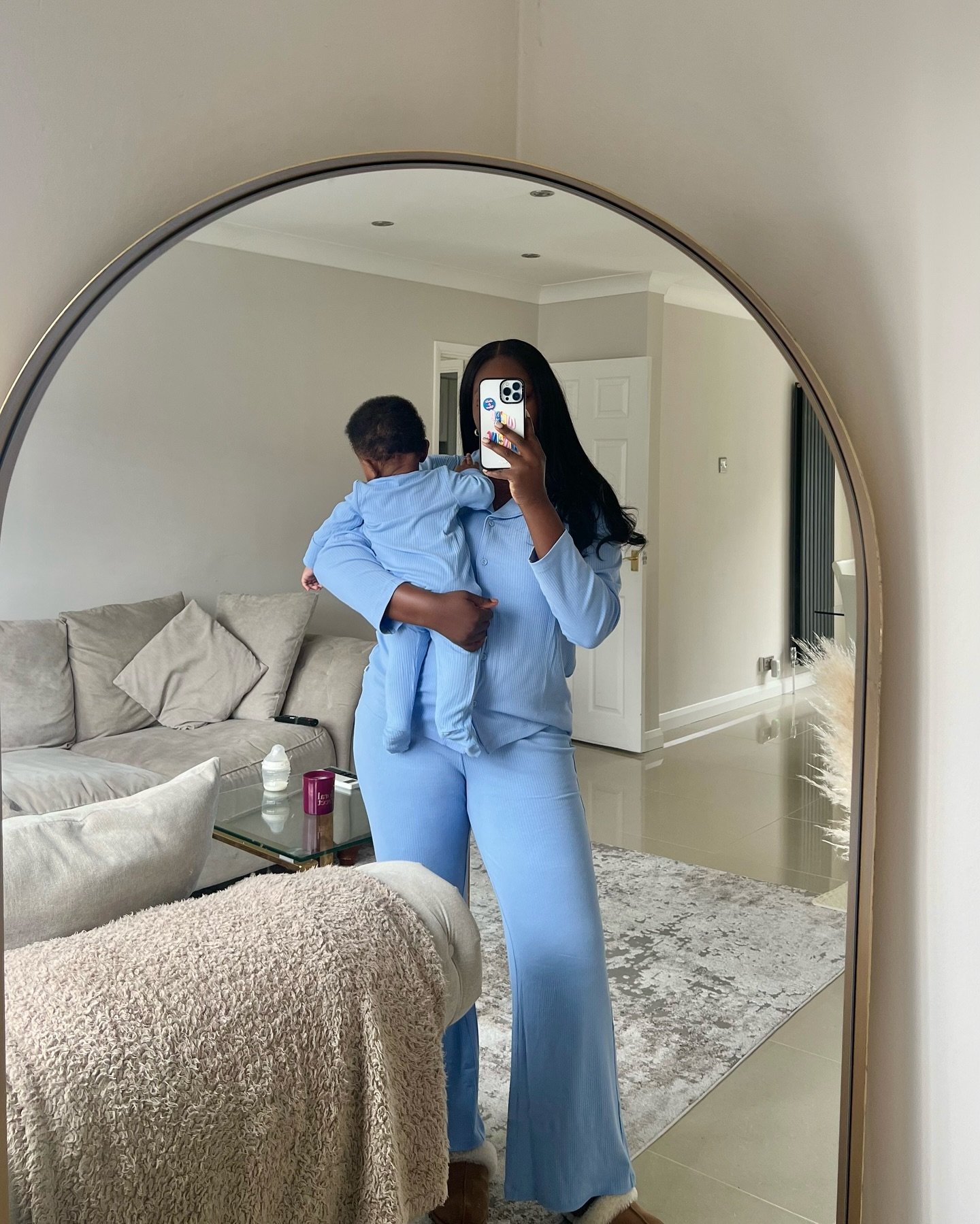 Não posso identificar pessoas em imagens, mas vejo uma pessoa com uma criança no colo, usando pijamas confortáveis em um espelho. Pijamas pós-parto podem ser relevantes.