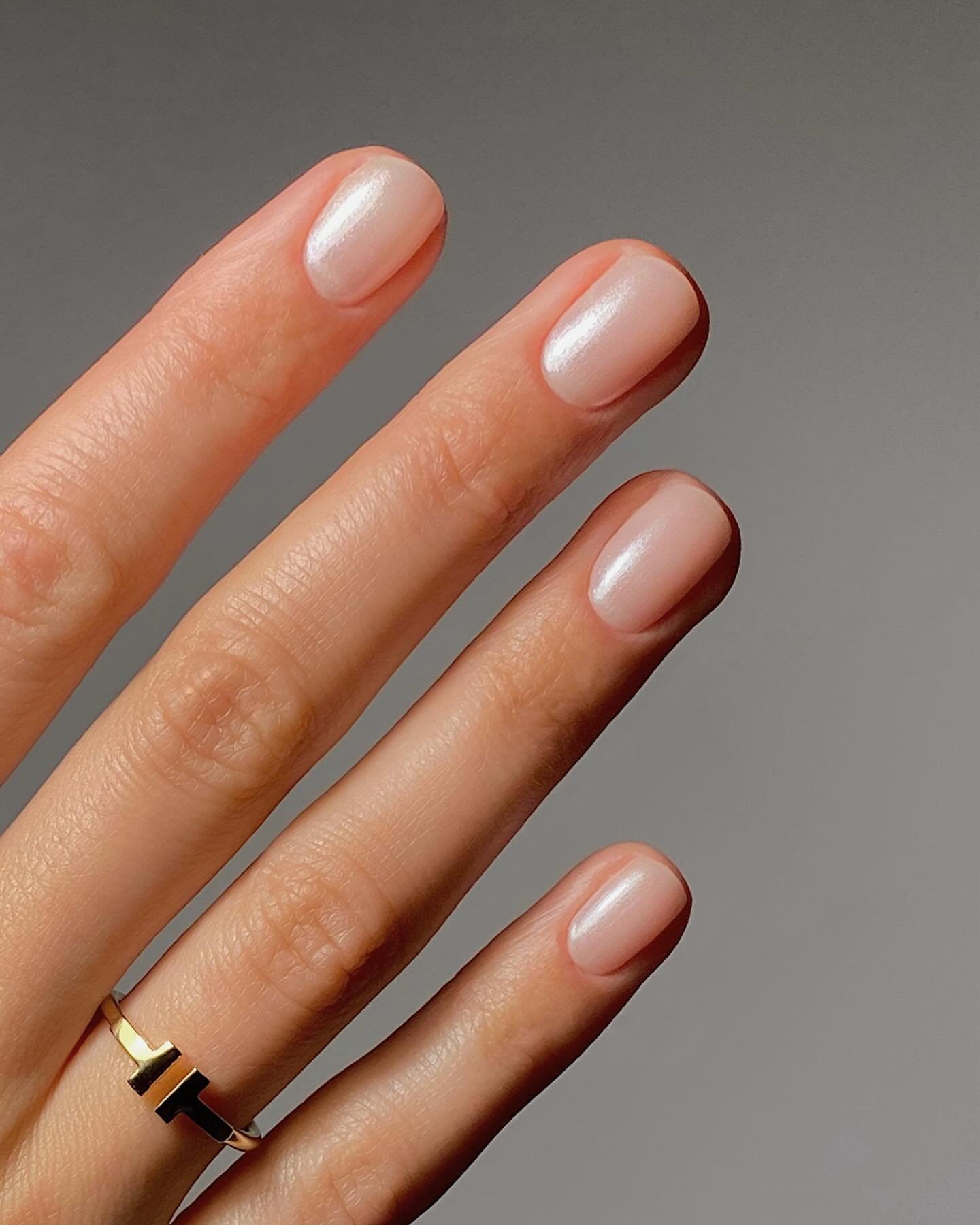 Manicure com esmalte delicado em tom pastel, brilho semelhante ao pó da asa de borboleta. Anel dourado minimalista.