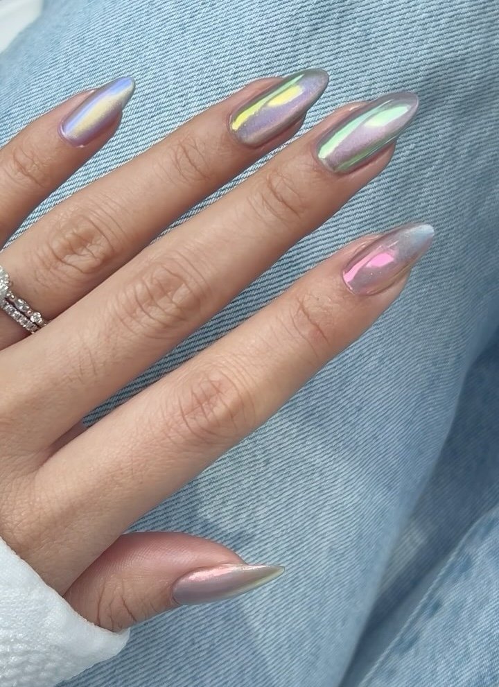 Unhas iridescentes com efeito de pó asa de borboleta sobre calça jeans.