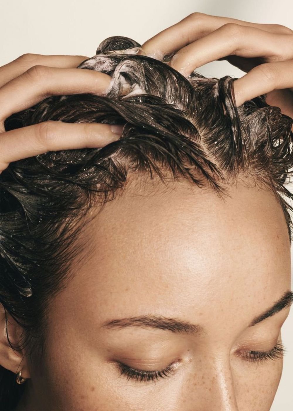 Mulher massageando cabelo ensaboado, possivelmente usando shampoo caseiro.