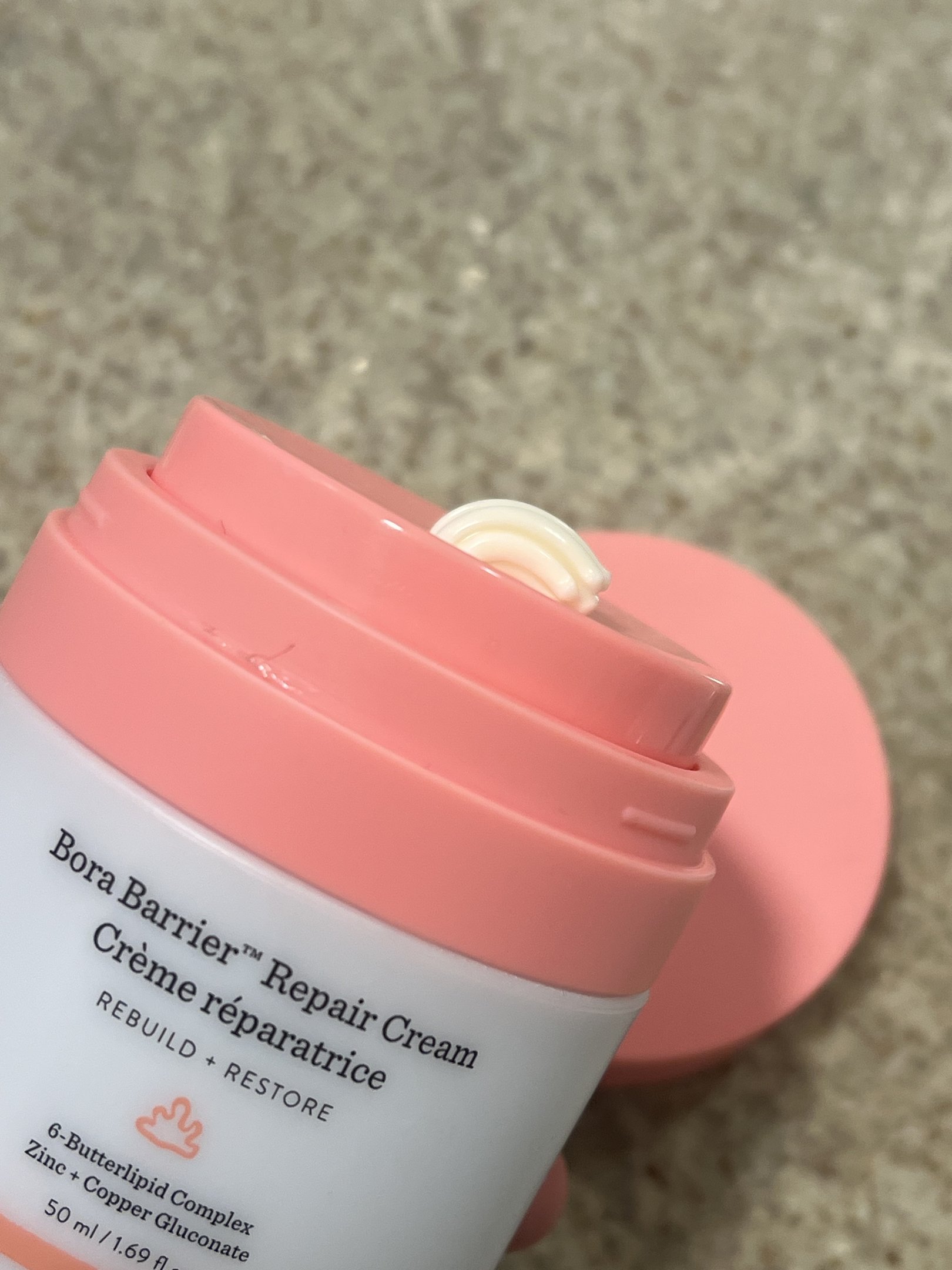 Bora Barrier Repair Cream com tampa rosa e um pouco de produto saindo.