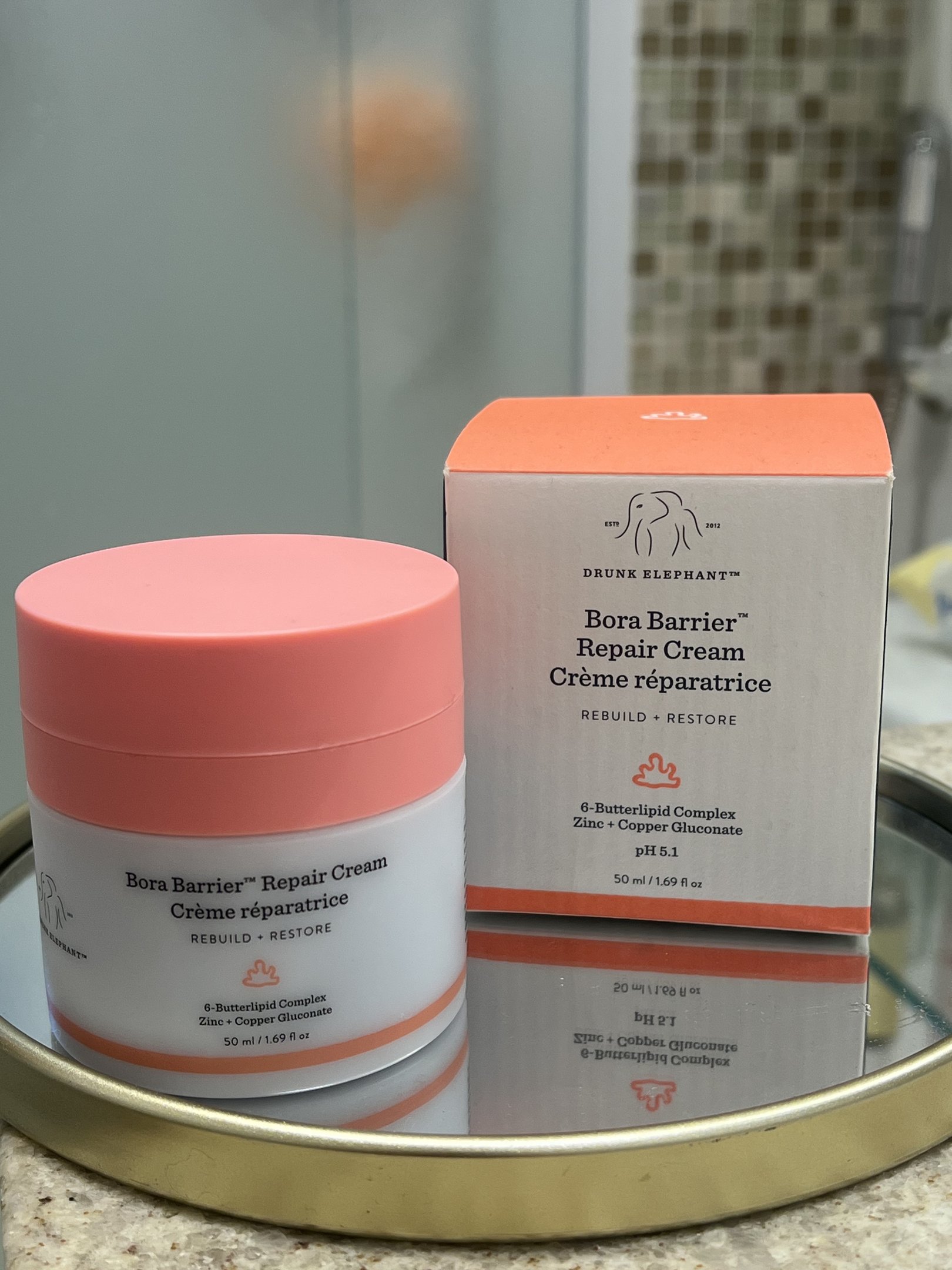 Bora Barrier Repair Cream em pote ainda na caixa sobre bandeja espelhada no banheiro.