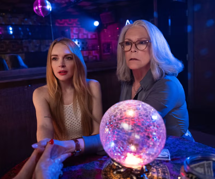 Duas mulheres em um bar místico, próximas a uma bola de cristal iluminada, em um ambiente misterioso.