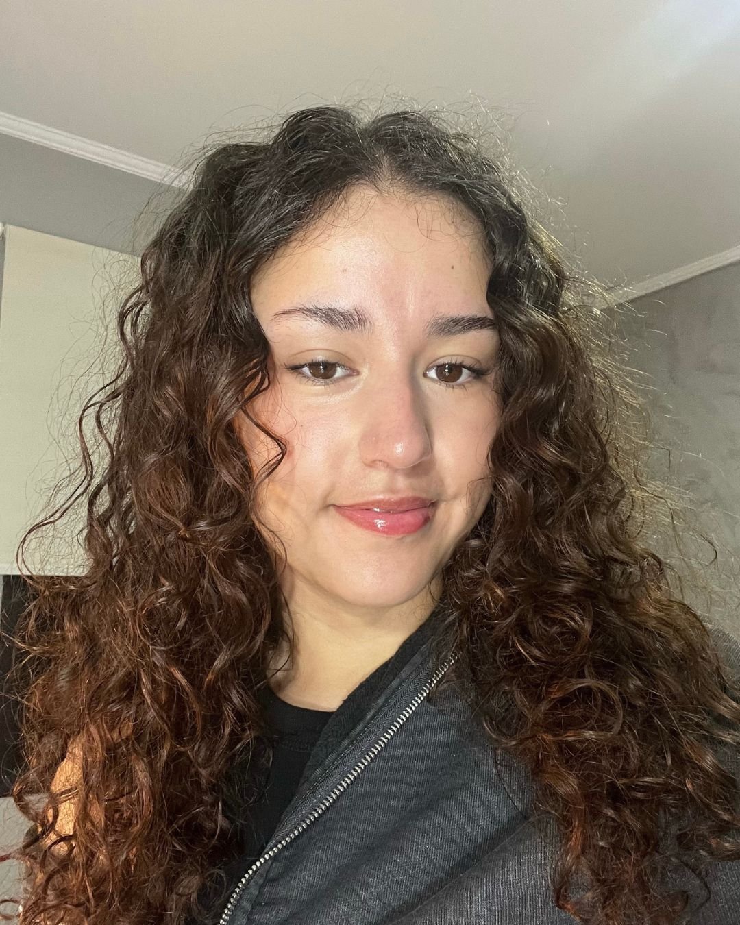 Pessoa com cabelo cacheado, resultado do uso de leave-in multibenefícios, sorrindo suavemente.