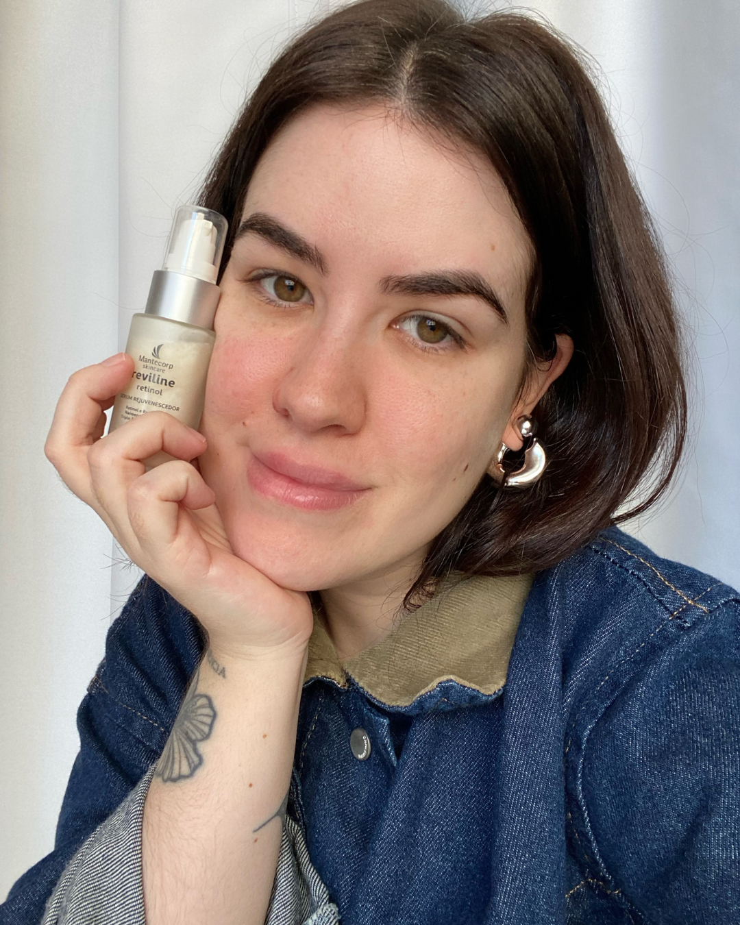 Pessoa segura um frasco do sérum com retinol Reviline da Mantecorp, sorrindo suavemente, com o cabelo escuro solto.