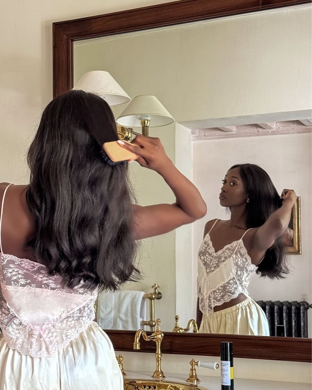 Mulher escovando o cabelo em frente ao espelho no banheiro, com expressão relaxada, sem rugas por estresse