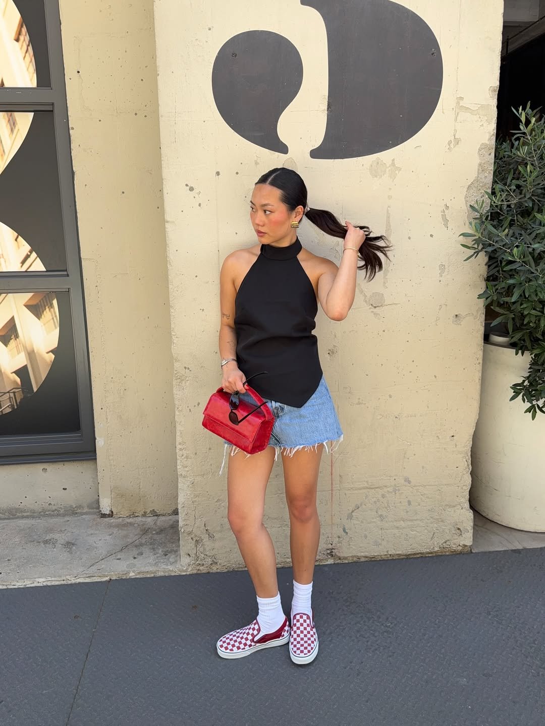 Mulher com saia curta jeans e bolsa vermelha, posando em pé.