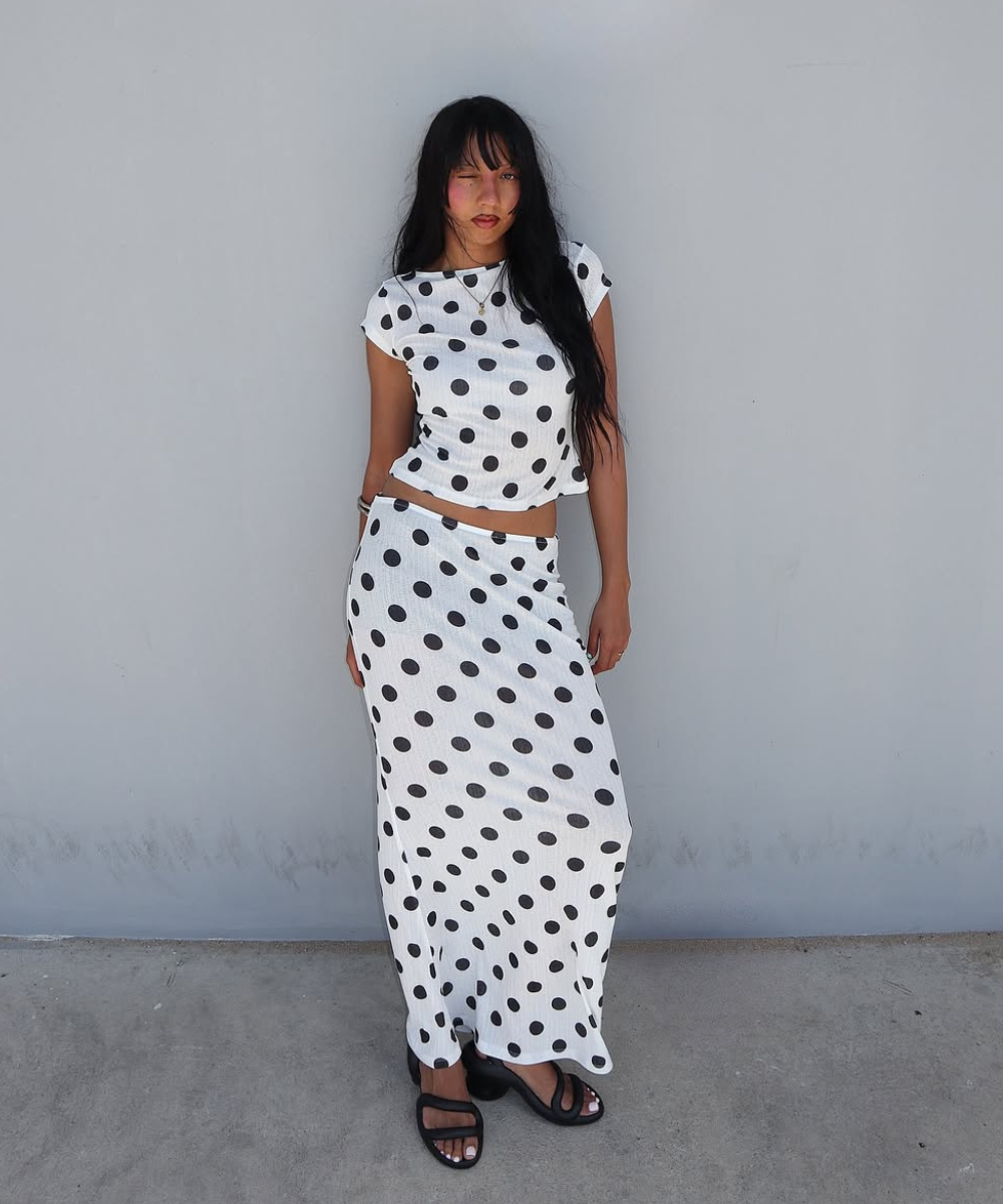 Pessoa posando com vestido de bolinhas em preto e branco, usando sandália preta estilosa.
