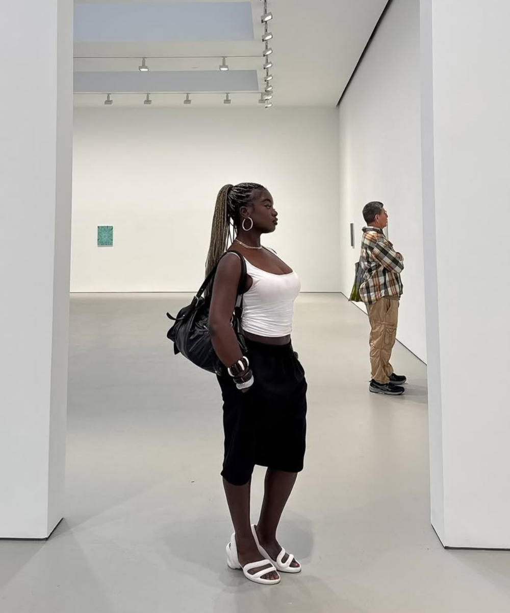 Pessoa com mochila e sandálias brancas em galeria de arte minimalista.