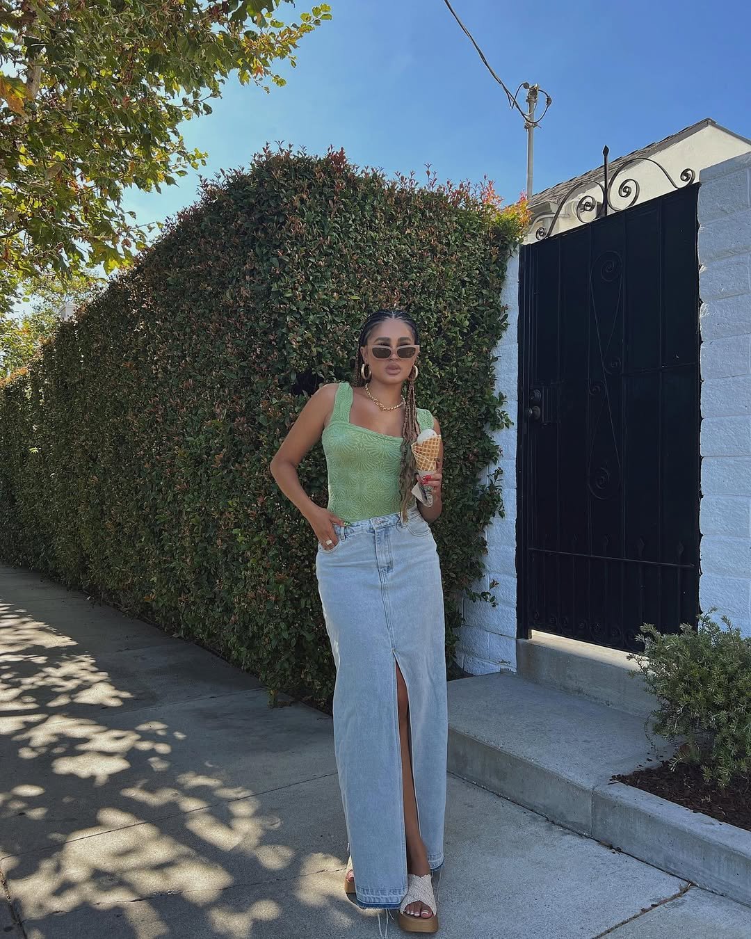 Pessoa com blusa verde e saia jeans, segurando sorvete, usando sandália de ráfia.