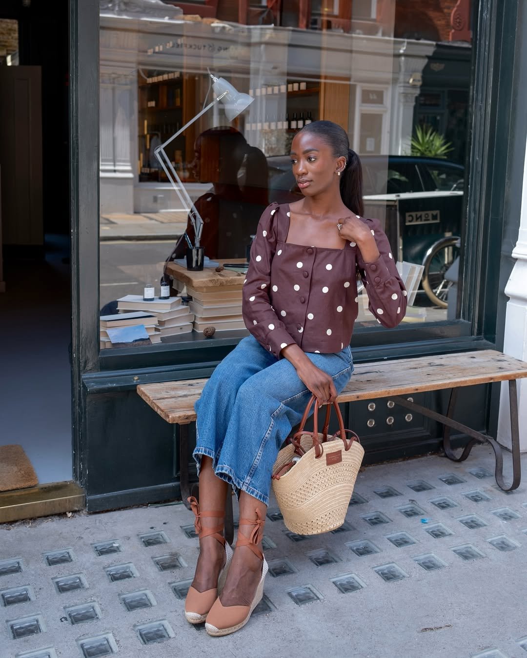 Pessoa sentada em um banco, usando jeans e blusa de bolinhas. Sapatos de salto da moda completam o visual.