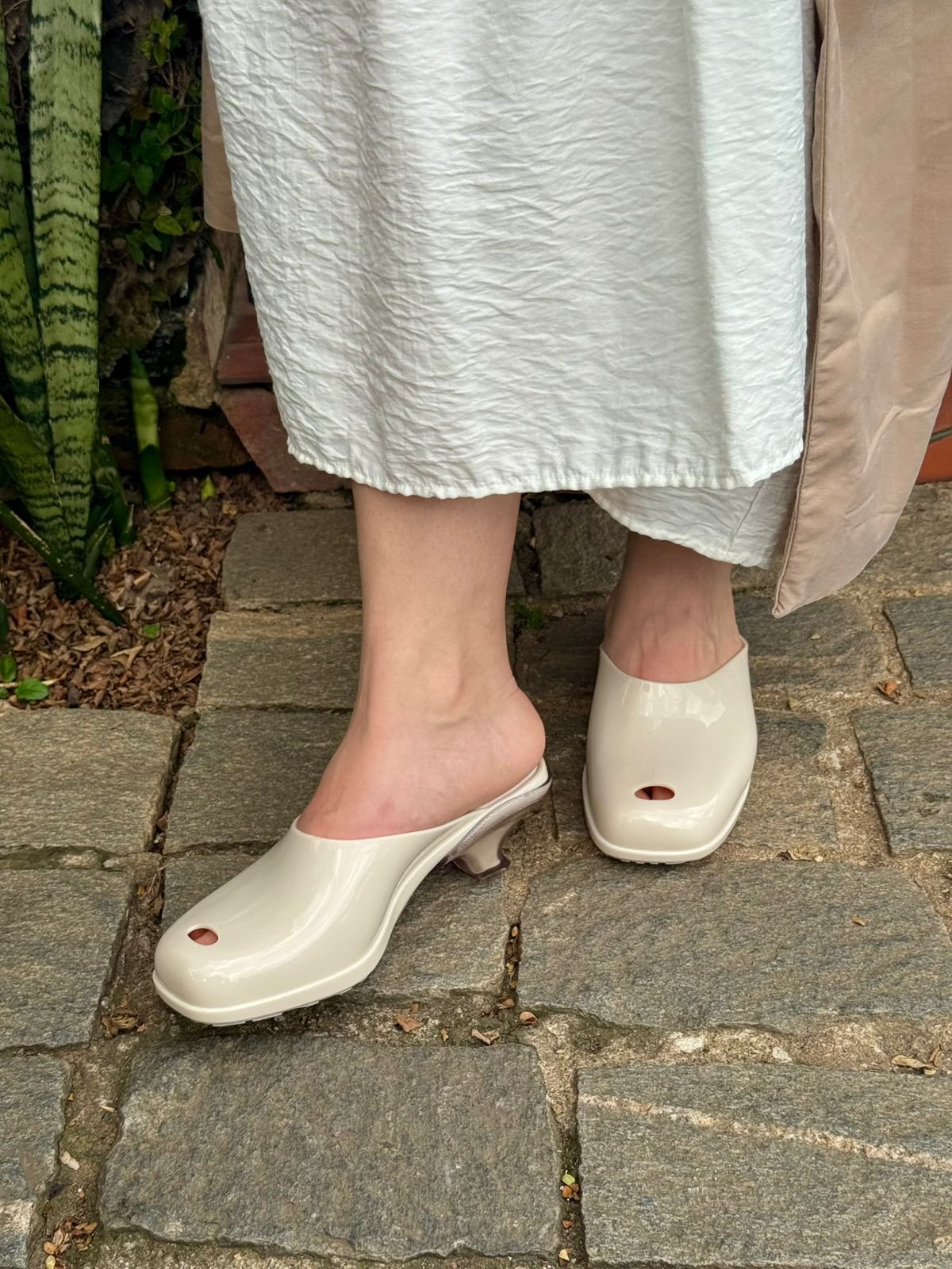 Pessoa usando sapato mule off white, uma das cores de sapato que vão bombar no verão de 2026, em piso de pedra.