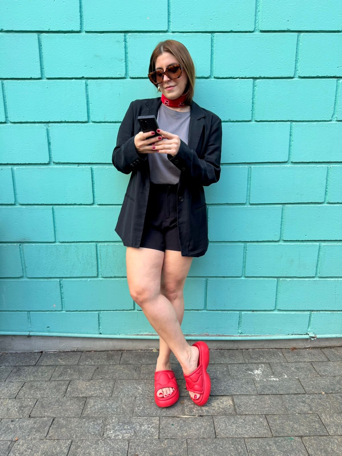 Mulher em pose casual com blazer preto, chinelos vermelhos, uma das cores de sapato que vão bombar no verão de 2026