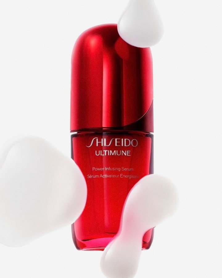 Sérum Shiseido Ultimune em frasco vermelho brilhante, cercado por gotas brancas flutuantes.