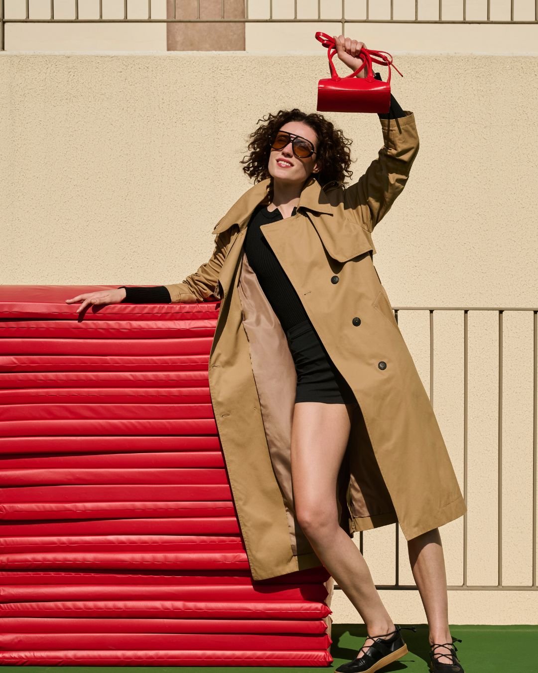 Mulher segura bolsa vermelha, usando sobretudo bege e sandália, em pose elegante e descontraída. mostrando como ficar chique e confortável com a nova coleção de renner