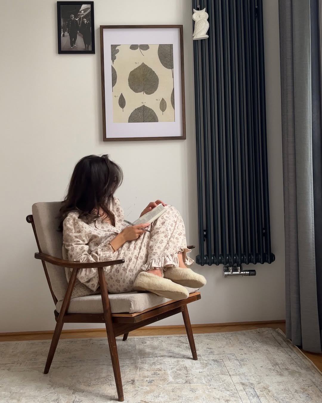 Mulher em pijama lendo silenciosamente em uma cadeira estofada, com quadros na parede ao fundo. Ilustrando o silêncio nas relações.