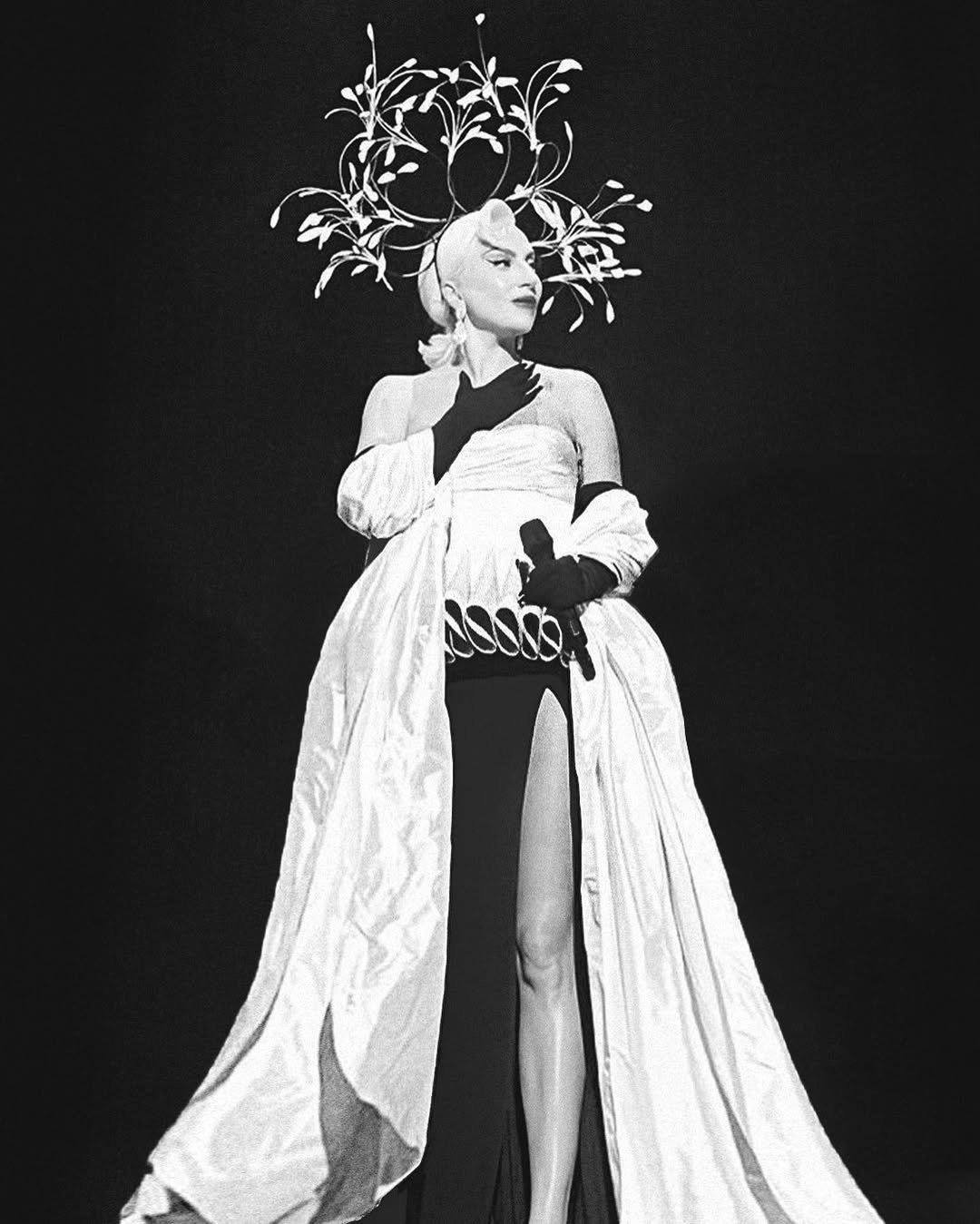Lady Gaga em vestido elegante com fenda alta e elaborada peça de cabeça inspirada em Schiaparelli.