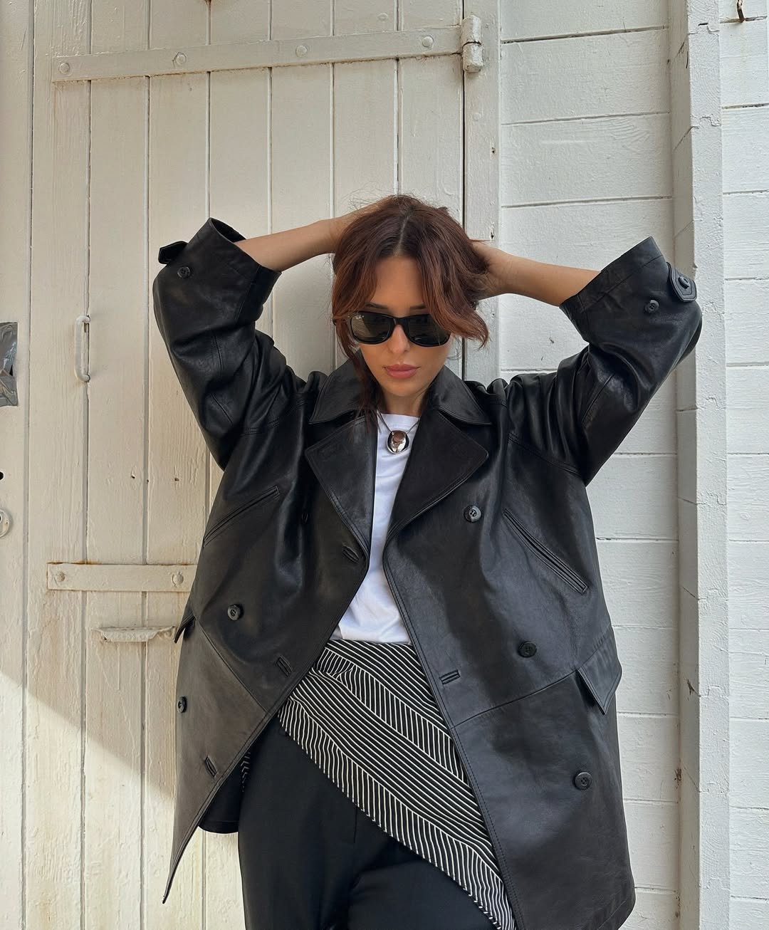 Mulher vestindo uma jaqueta de couro preta com um lenço amarrado na cintura e óculos de sol.