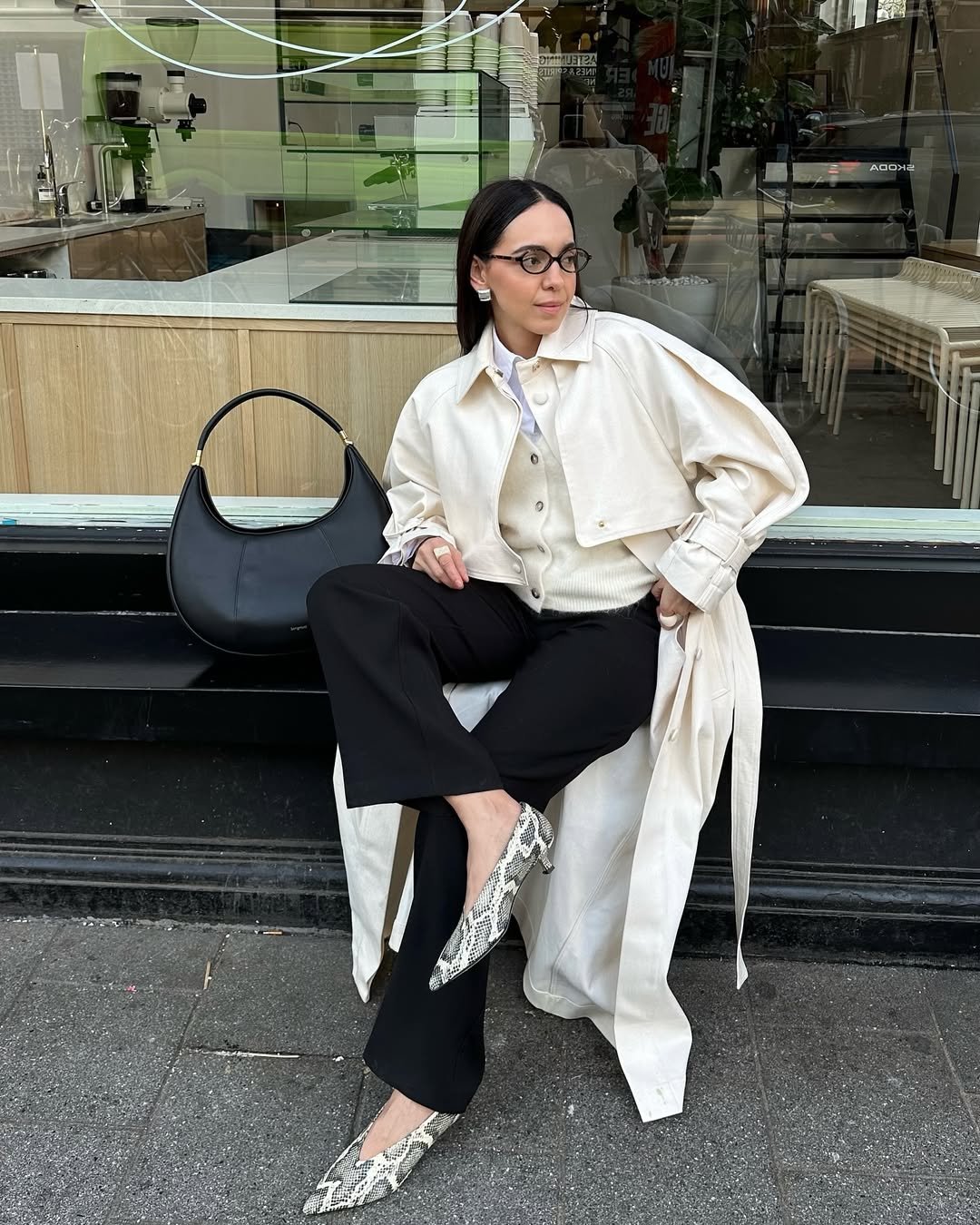 Mulher sentada com roupas elegantes, usando sapatos de salto baixo com estampa de cobra.