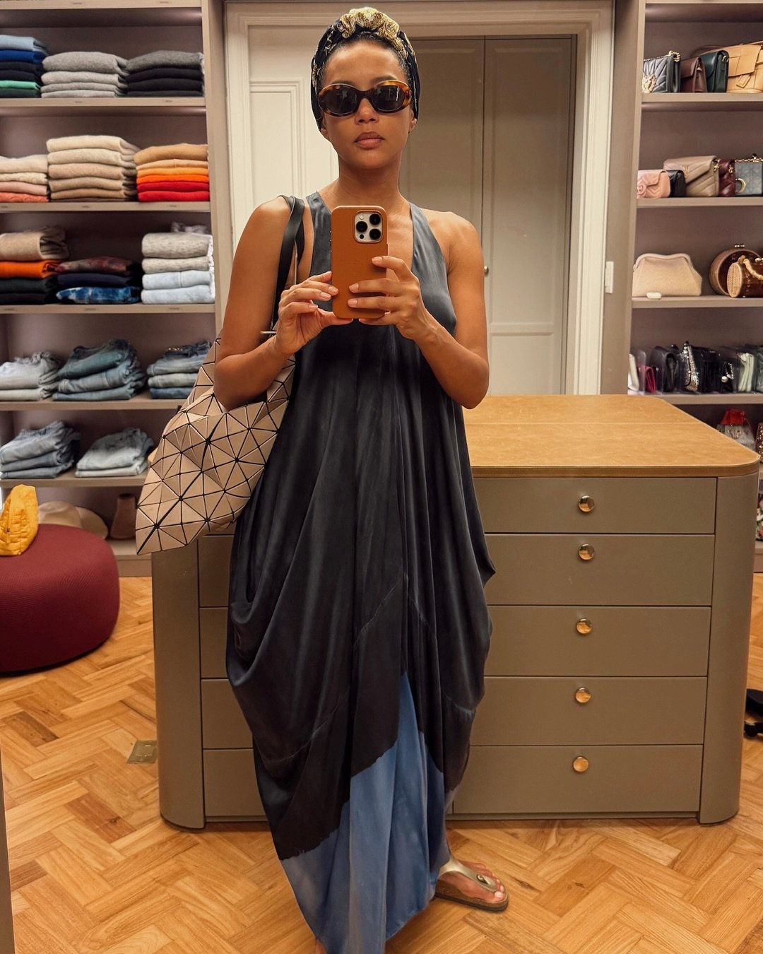 Taís Araújo em foto no espelho vestindo um vestido azul escuro e uma bolsa bege com óculos de sol.