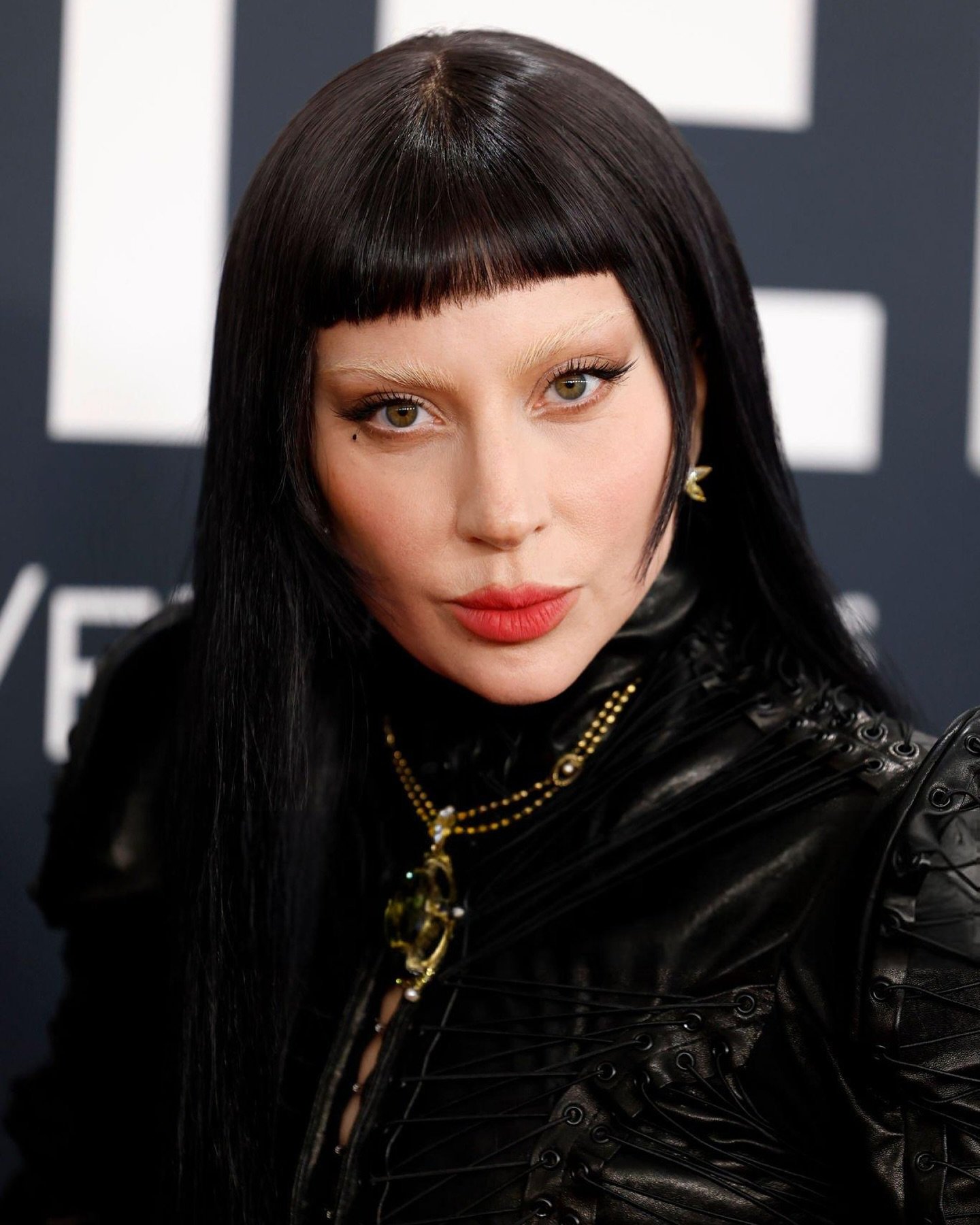 Pessoa com cabelo escuro e franjas curtas. Suas sobrancelhas descoloridas contrastam com o batom vermelho.