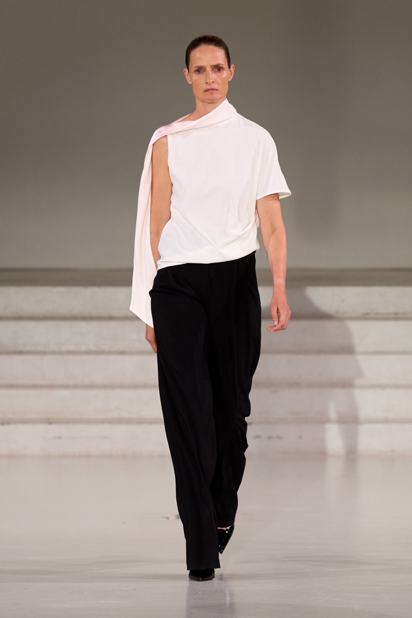 Modelo usa blusa assimétrica branca e calça preta na passarela da Copenhagen Fashion Week 2026.