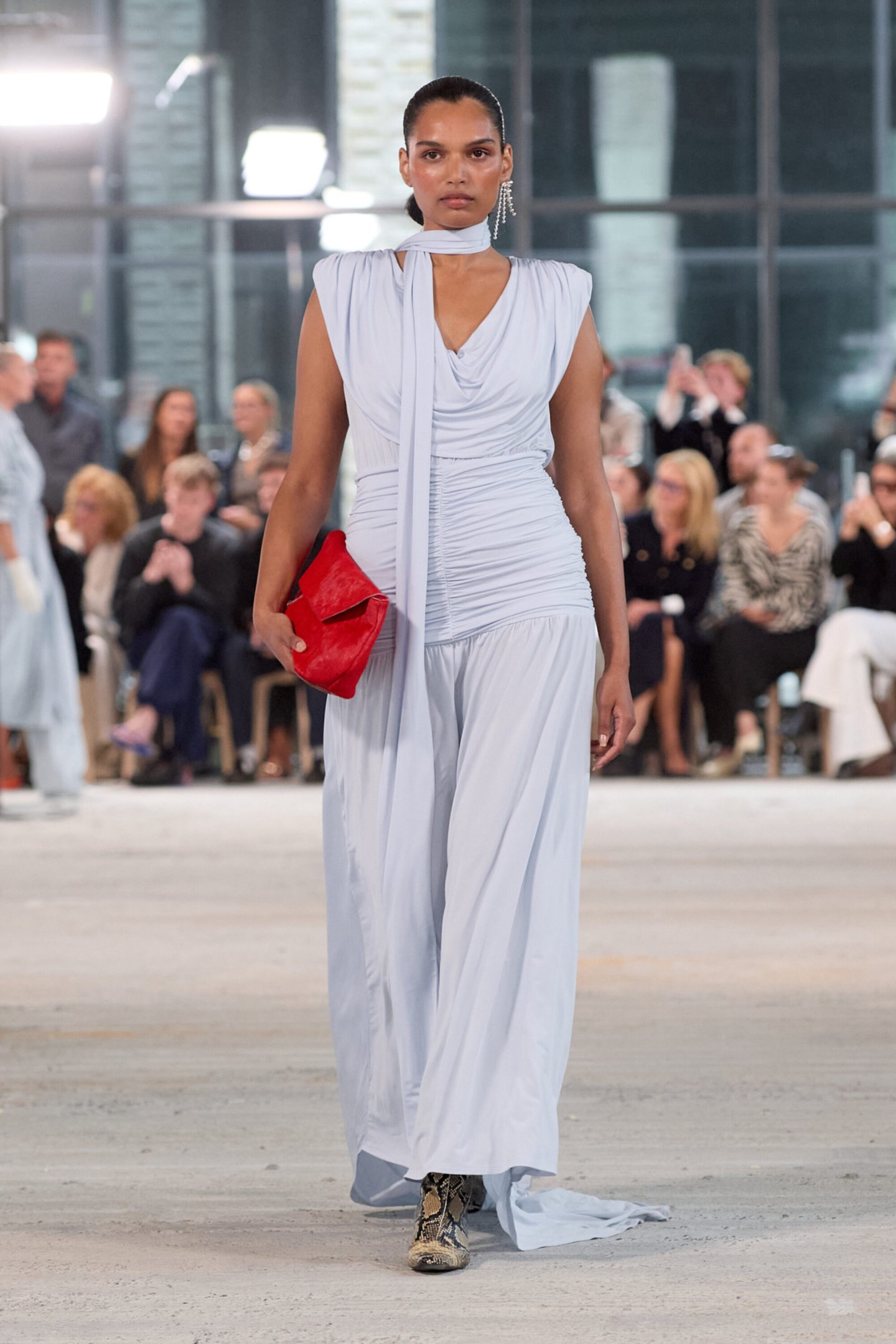 Modelo desfila com vestido azul claro e bolsa vermelha na Copenhagen Fashion Week Spring 2026. Público ao fundo.