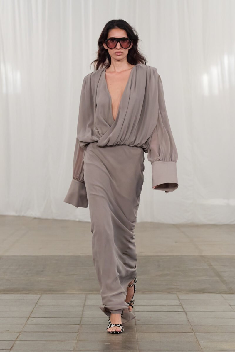 Modelo apresenta vestido cinza com decote profundo e mangas largas na passarela de moda primavera 2026.