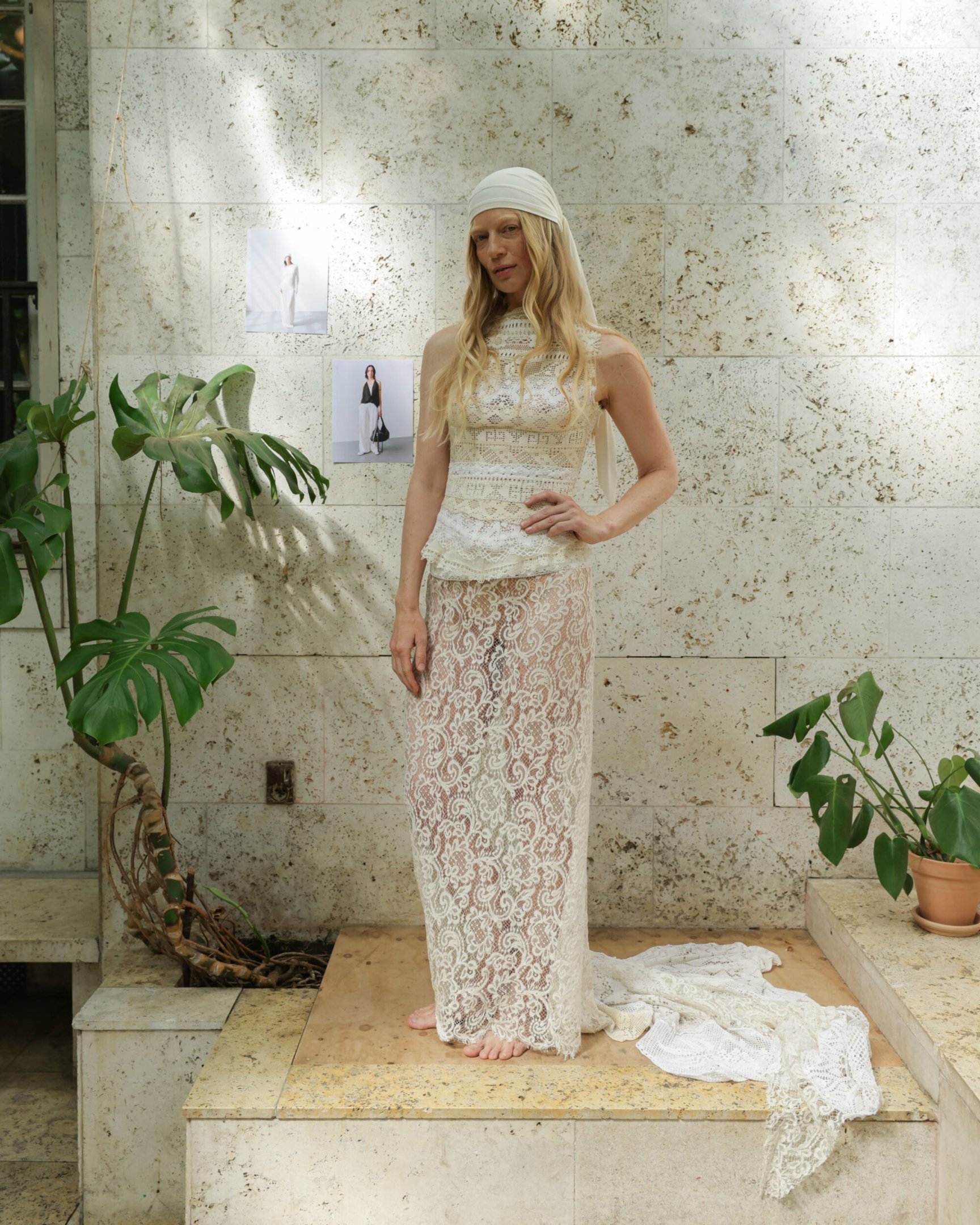 Loira com vestido rendado bege e bandana posa em cenário natural com plantas, evocando moda primavera Copenhagen 2026.