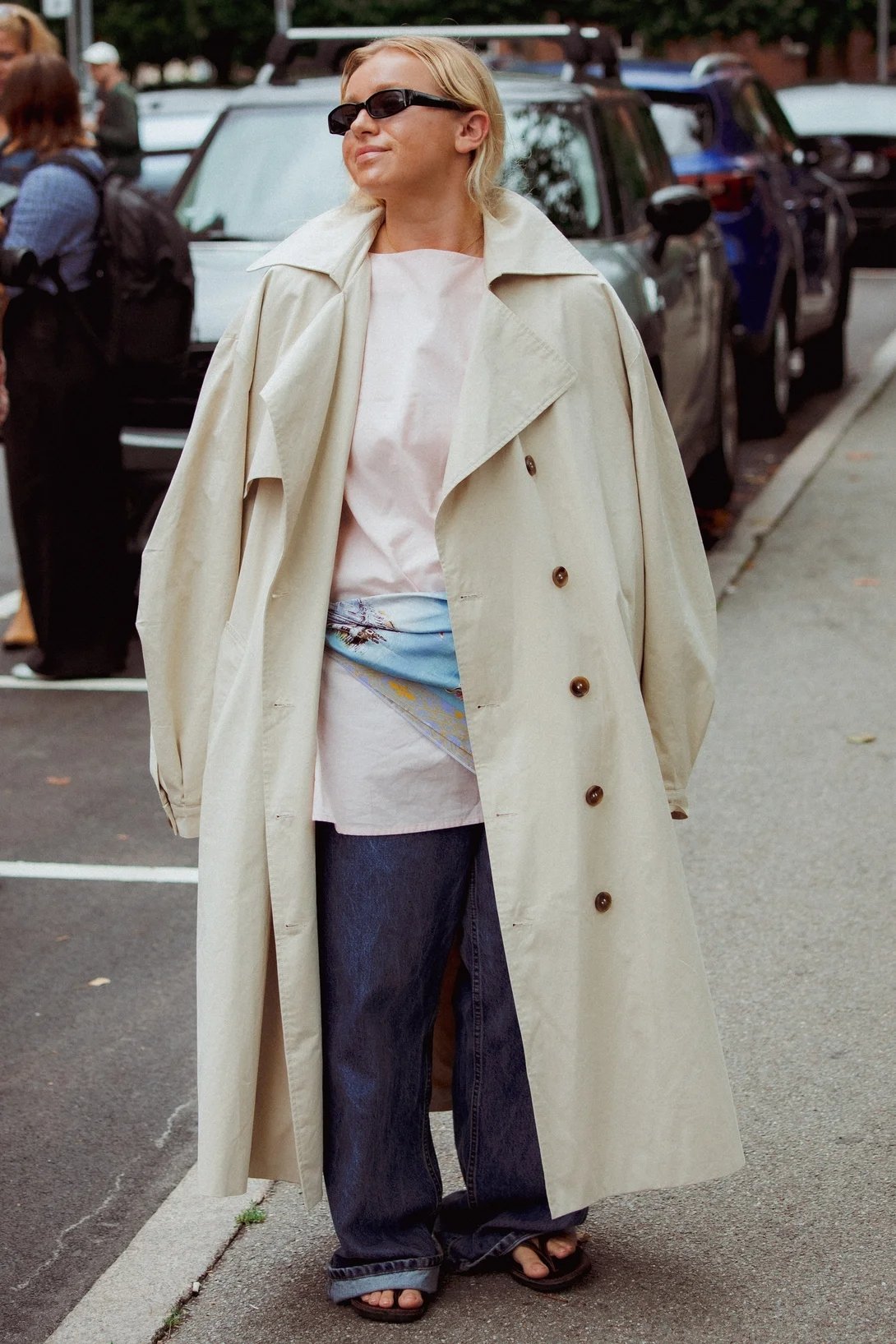 Pessoa usando trench coat bege, jeans largos e óculos escuros no street style da Copenhagen Fashion Week.