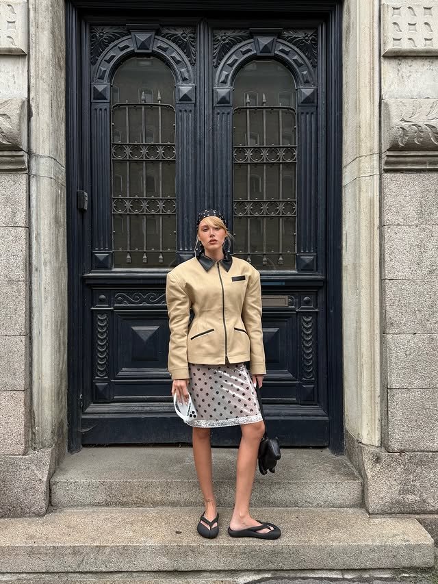Pessoa posando em frente a uma porta ornamentada, usando roupa moderna e elegante. Estilo urbano da Copenhagen Fashion Week.
