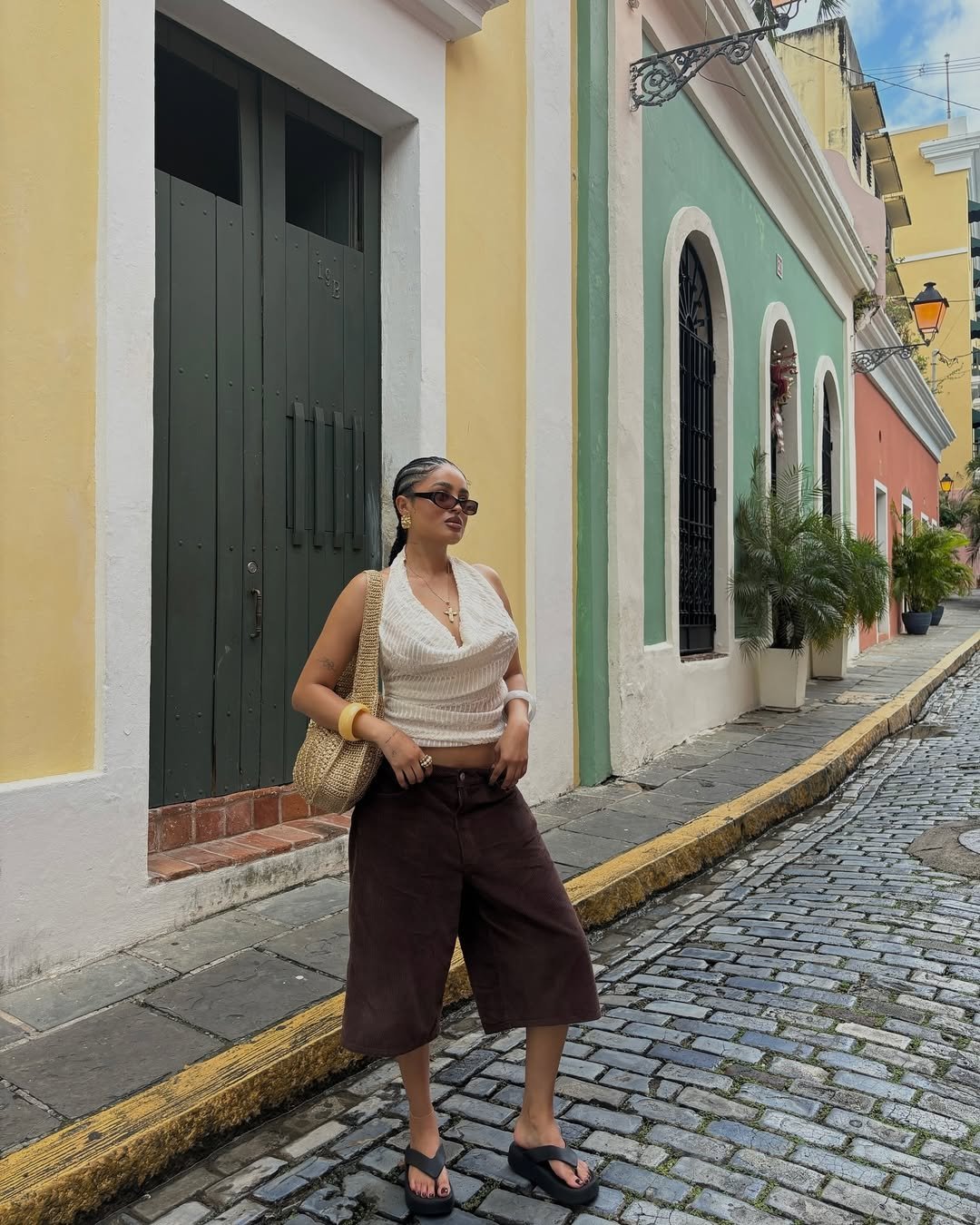 Mulher com blusa branca e bermuda marrom em rua colorida. Estilo reflete tendências verão 2026.