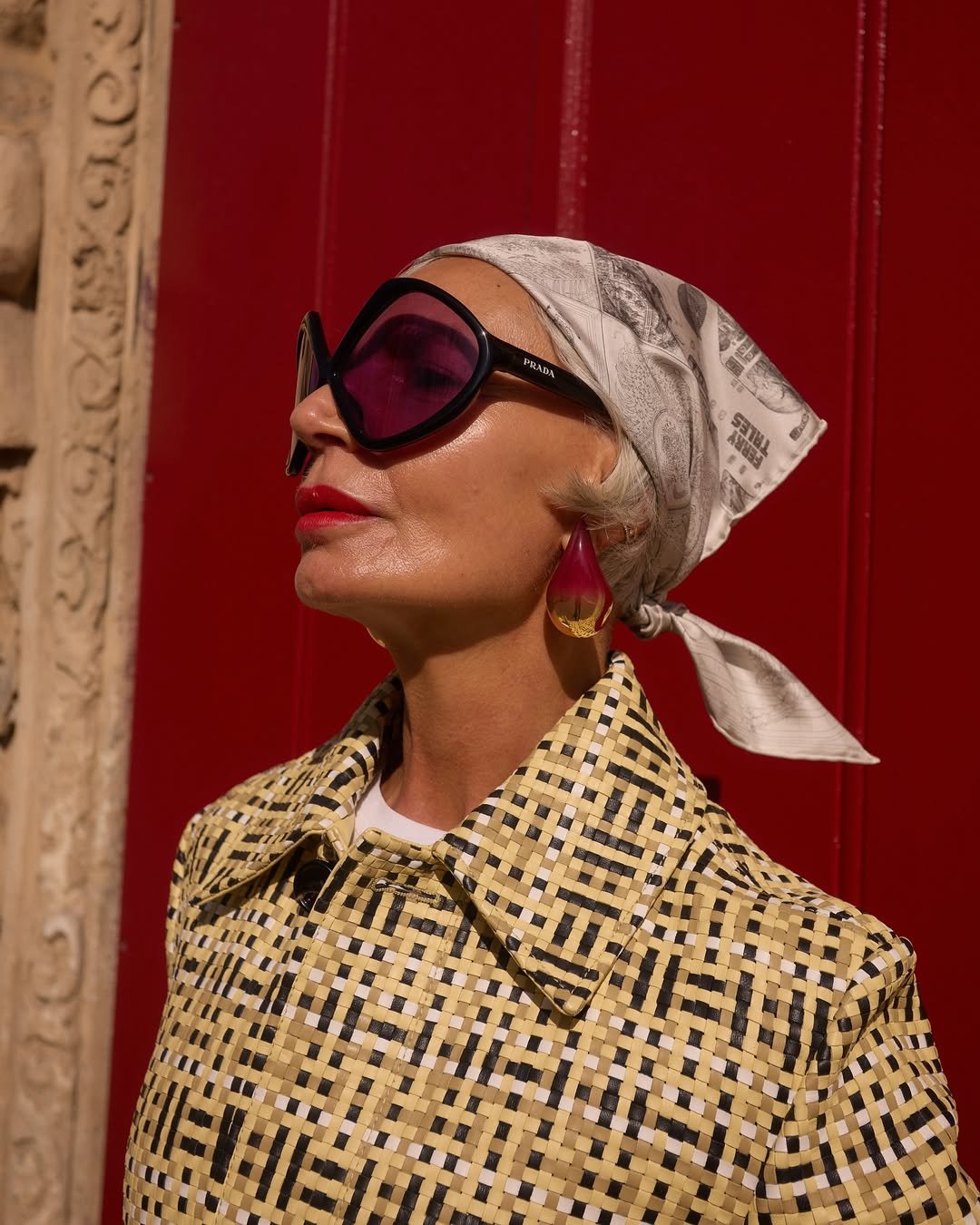 Mulher de lenço e óculos grandes aprecia um dia de sol, destacando tendências verão 2026 com acessórios elegantes e estilo retrô.