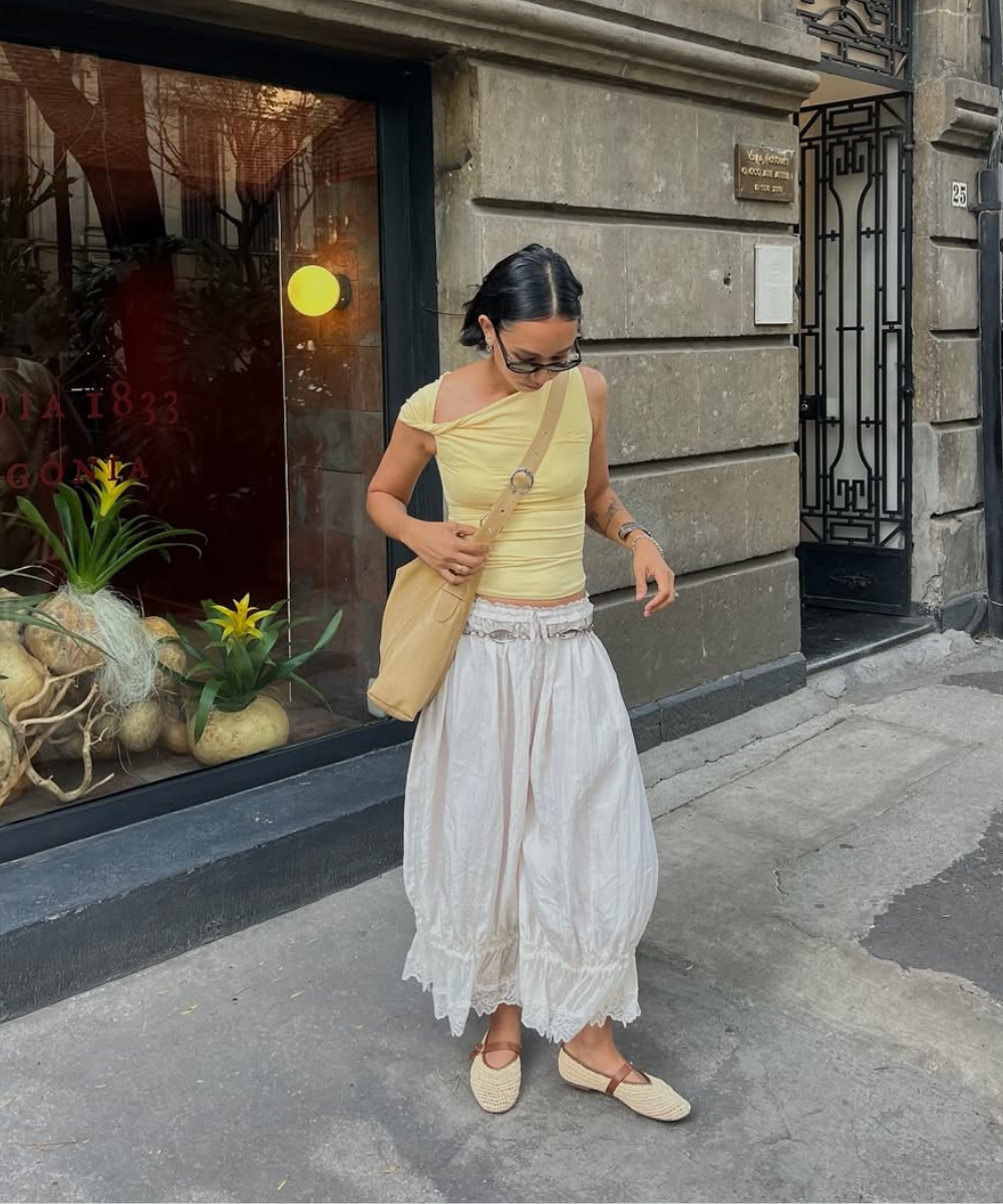 Pessoa usando calça bloomer branca e blusa amarela, com bolsa bege, em frente a uma loja.