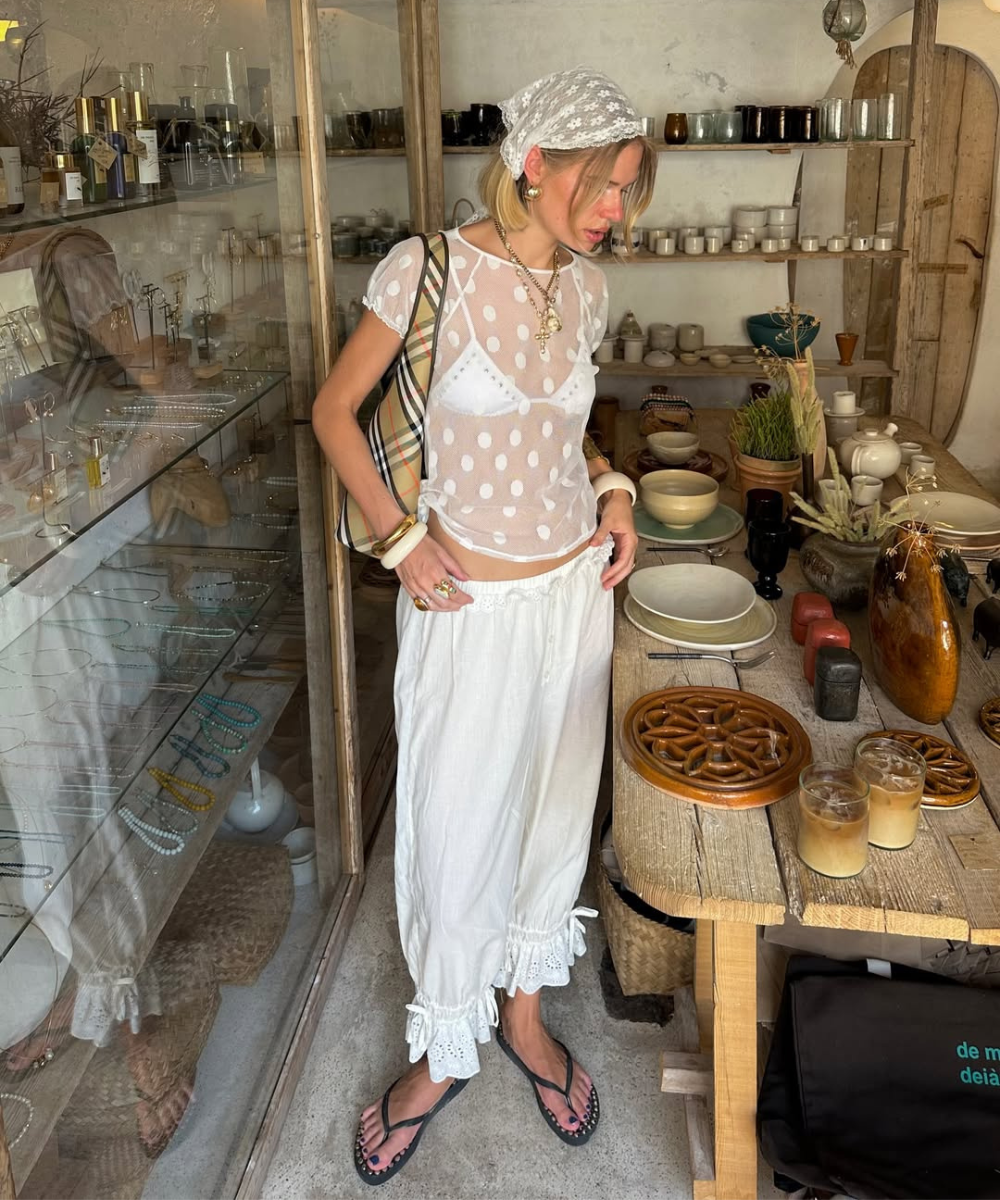 Pessoa vestindo calça bloomer branca e blusa transparente de bolinhas, em uma loja de objetos artesanais.