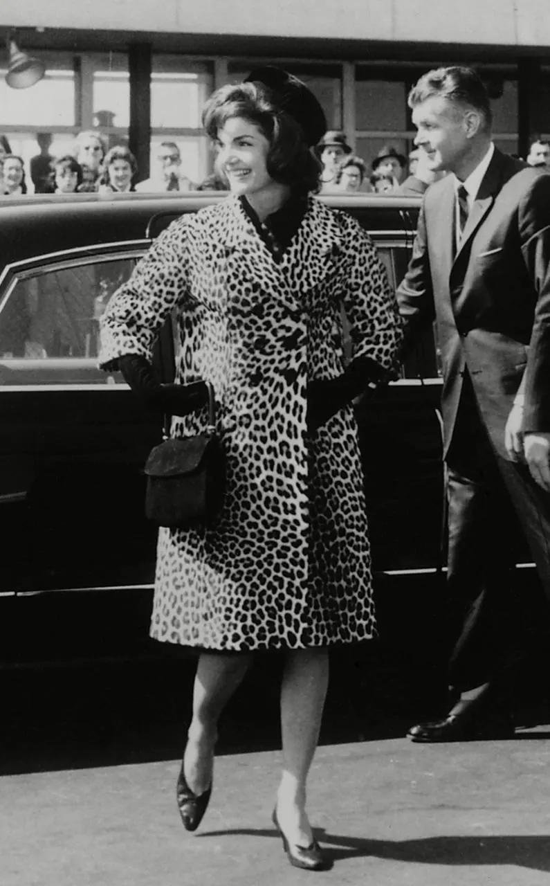 Mulher com casaco de estampa de leopardo saindo de um carro, cercada por uma multidão.