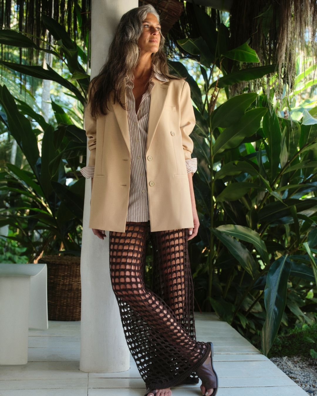 Modelo com blazer bege e calça rendada em cenário tropical, incorporando tendências de primavera verão.
