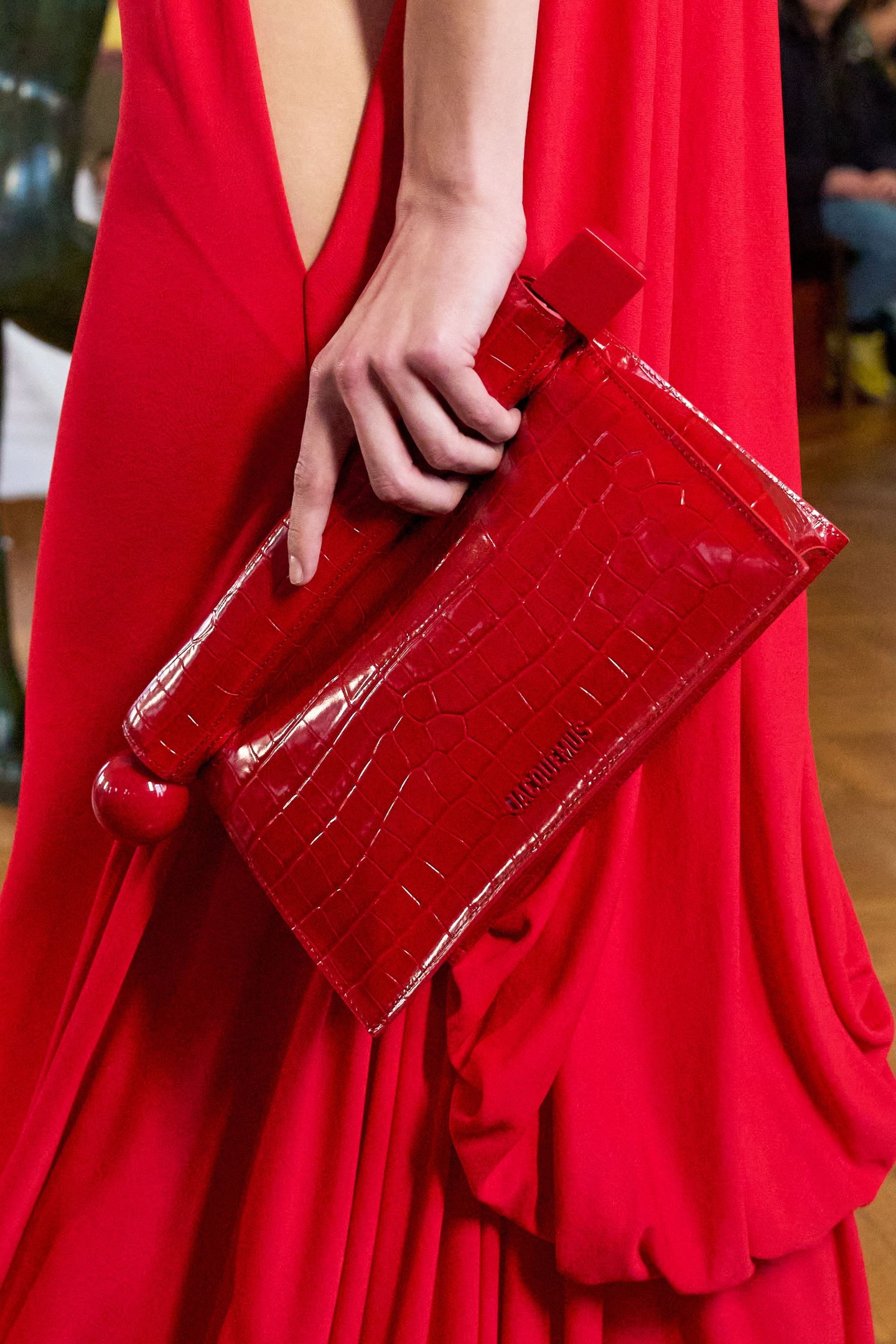 Vestido vermelho intenso com bolsa de couro texturizada no mesmo tom nas mãos de uma pessoa.